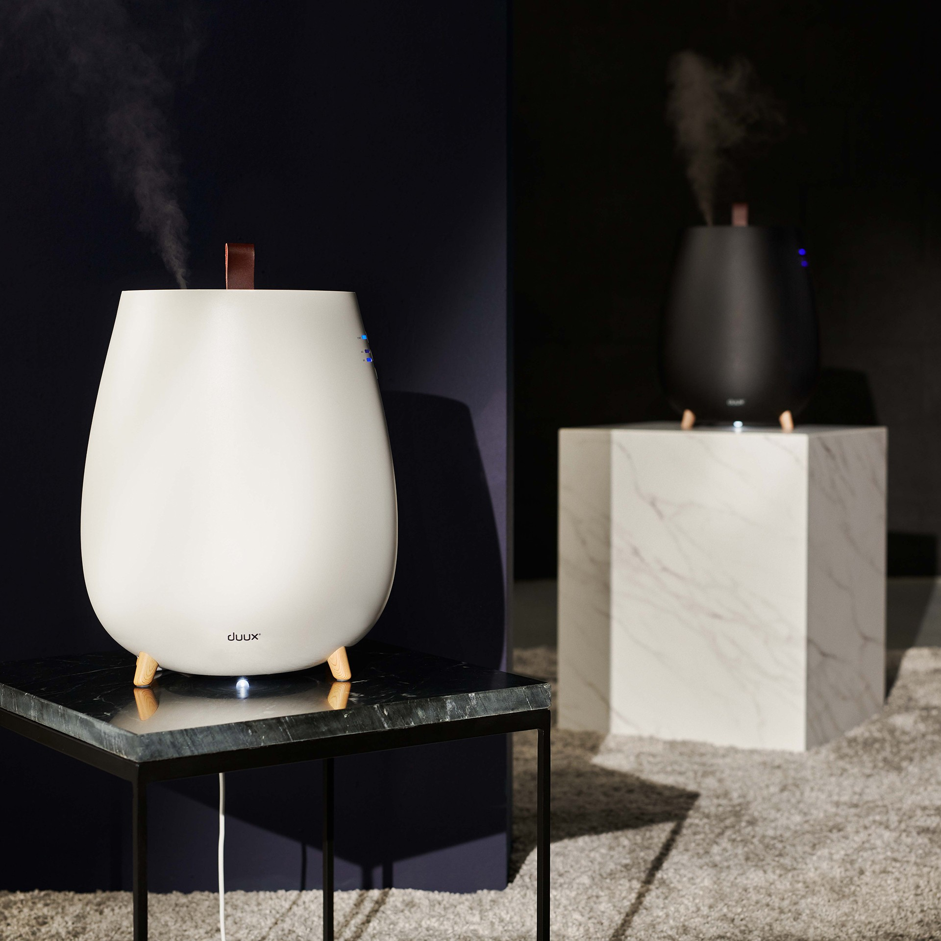 Białe i czarne nawilżacze na ciemnym tle. Jeden na marmurowej kostce, drugi na stole.