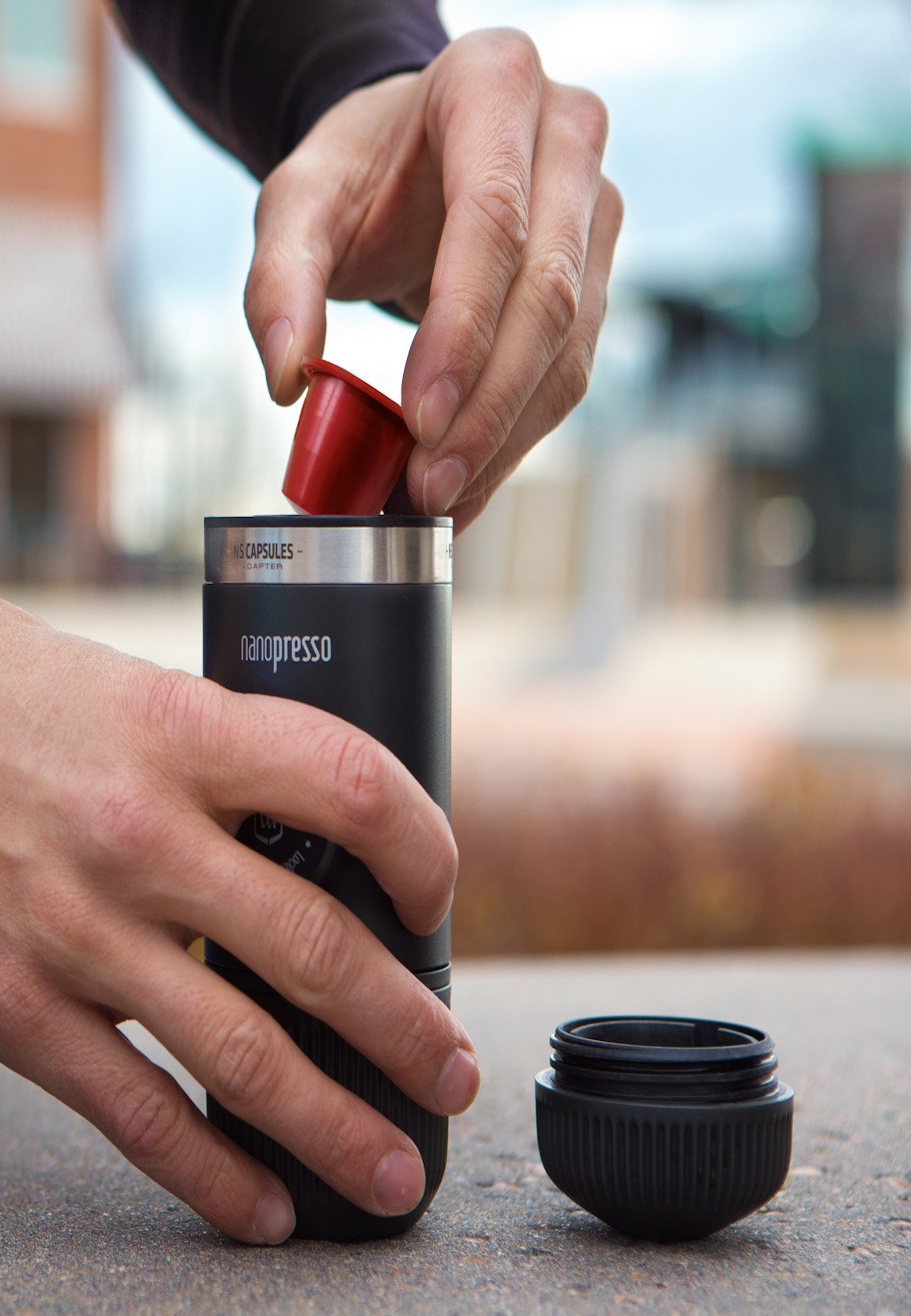 Hände, die eine rote Kapsel in einen schwarzen tragbaren Espressomaschine legen.