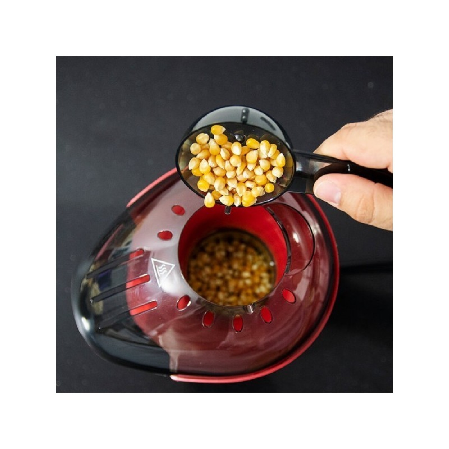 Una mano sta versando chicchi di popcorn da una paletta nera in una macchina per popcorn rossa.
