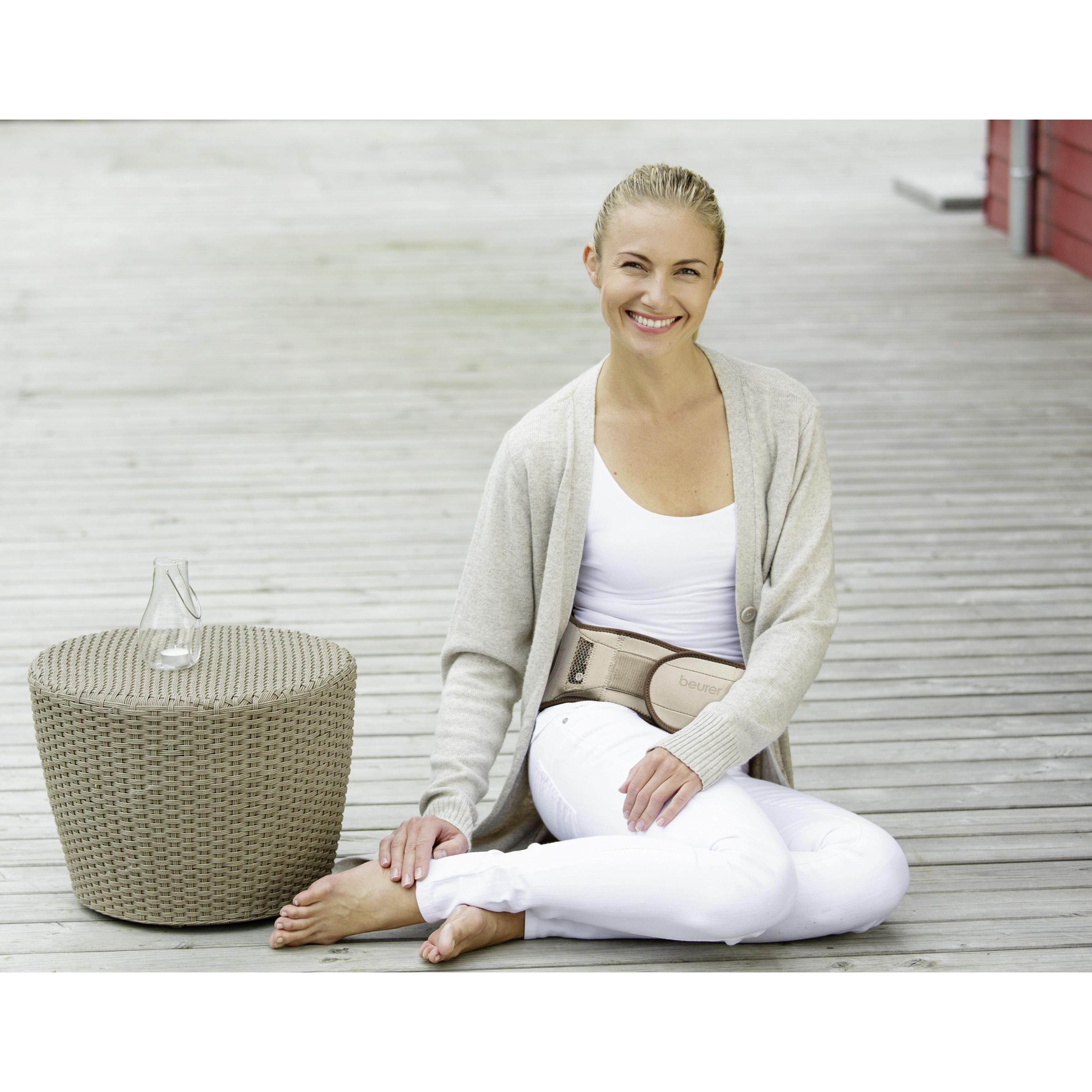 Donna con cardigan beige e pantaloni bianchi, seduta su un ponte di legno, sorridente.