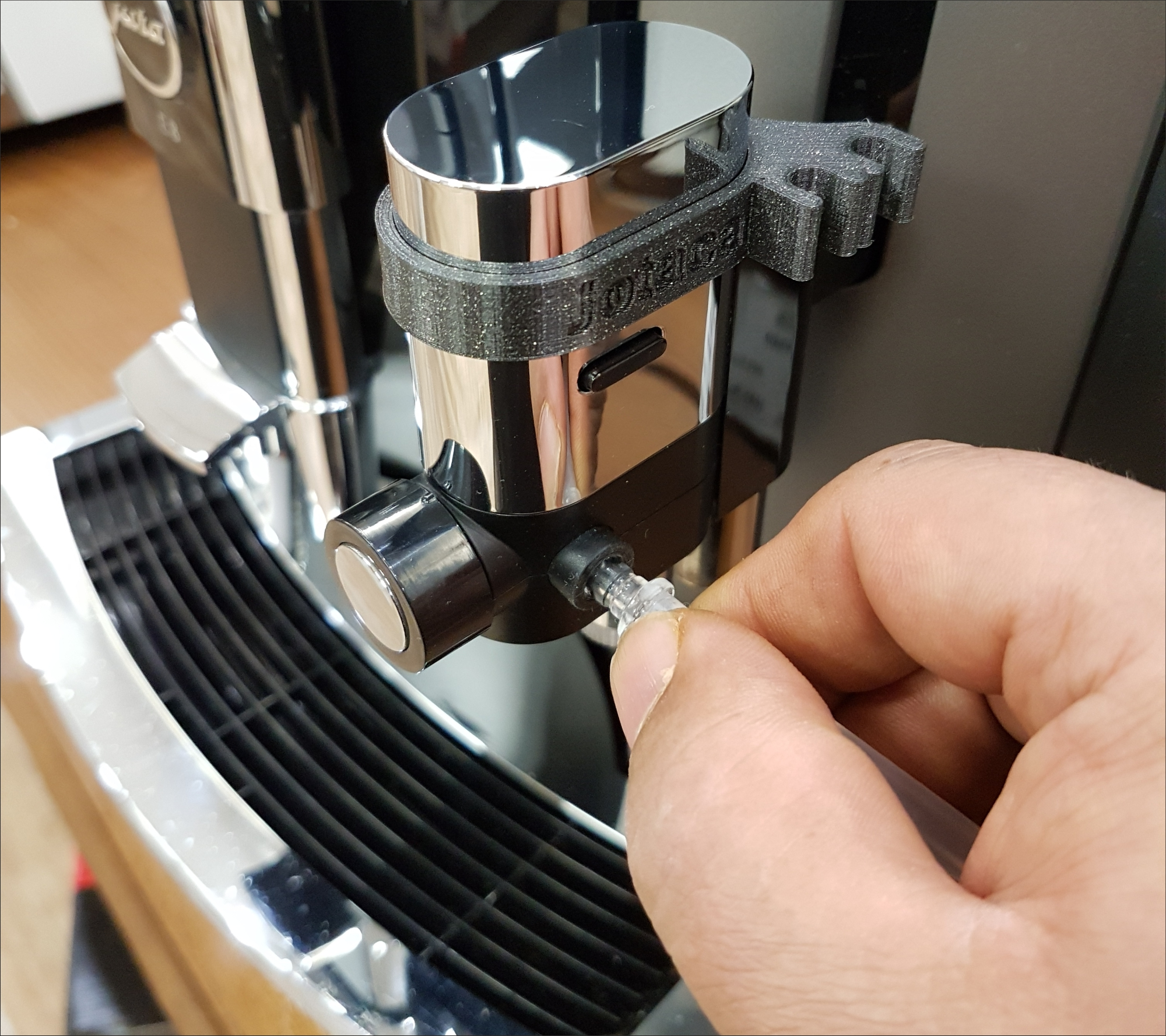 Die Hand einer Person verbindet einen durchsichtigen Schlauch mit einer schwarzen Espressomaschine.