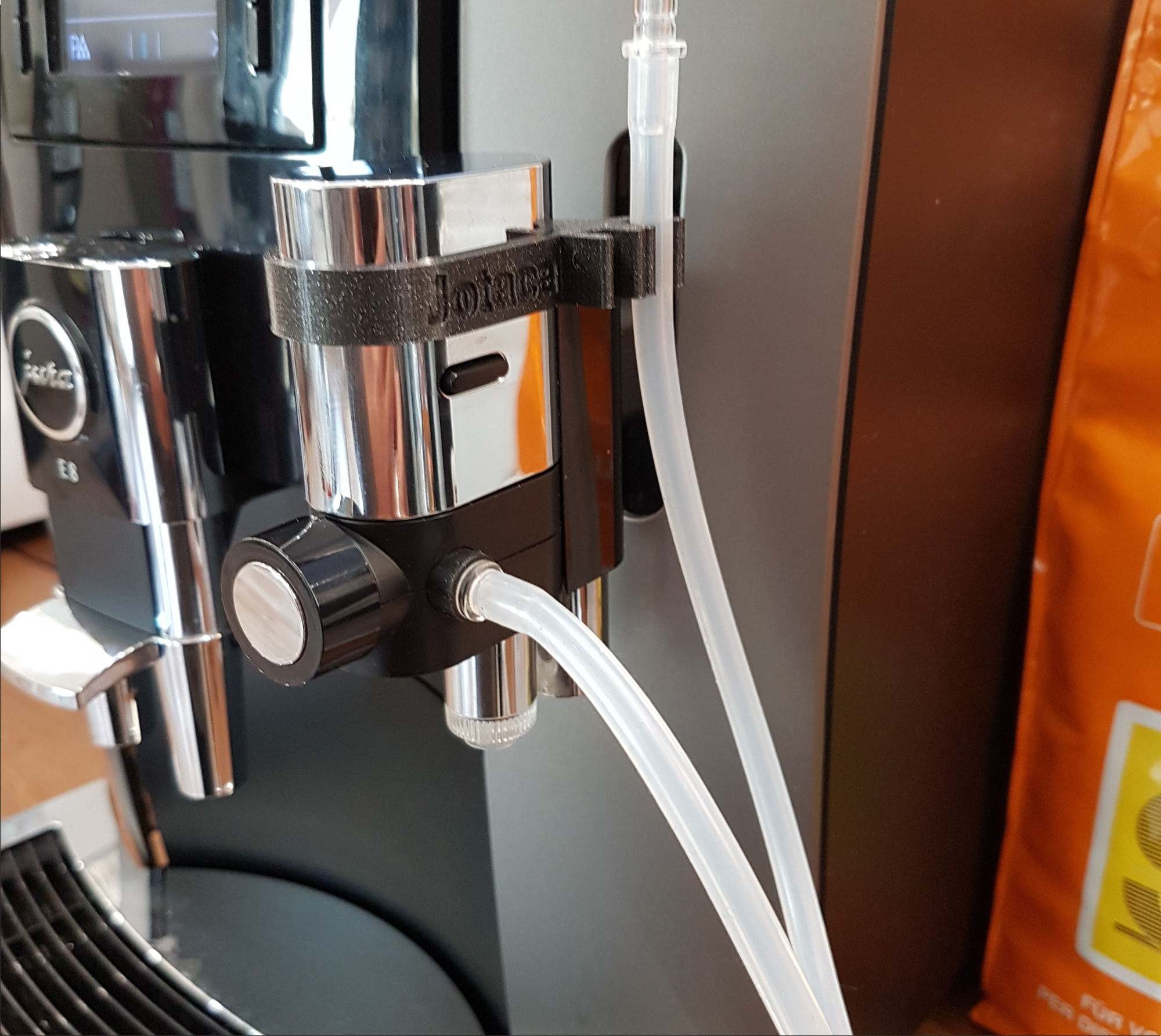 Nahaufnahme einer Kaffeemaschine mit angeschlossenem Zubehör, Schläuchen und einem schwarzen Bedienfeld.
