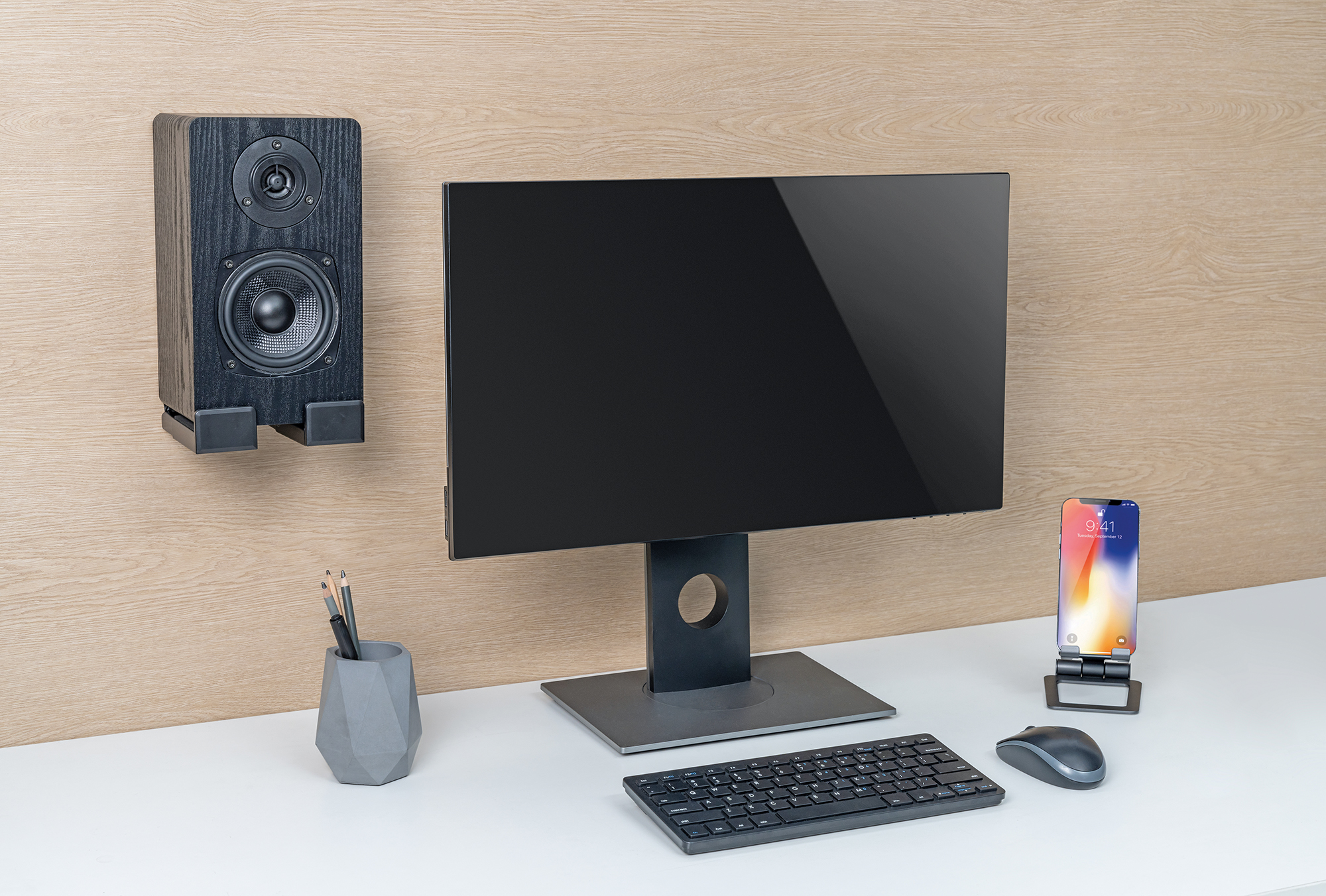 Ein Schreibtisch mit Monitor, Lautsprecher, Tastatur, Maus, Telefon und Stifthalter. Der Hintergrund ist Holzvertäfelung.