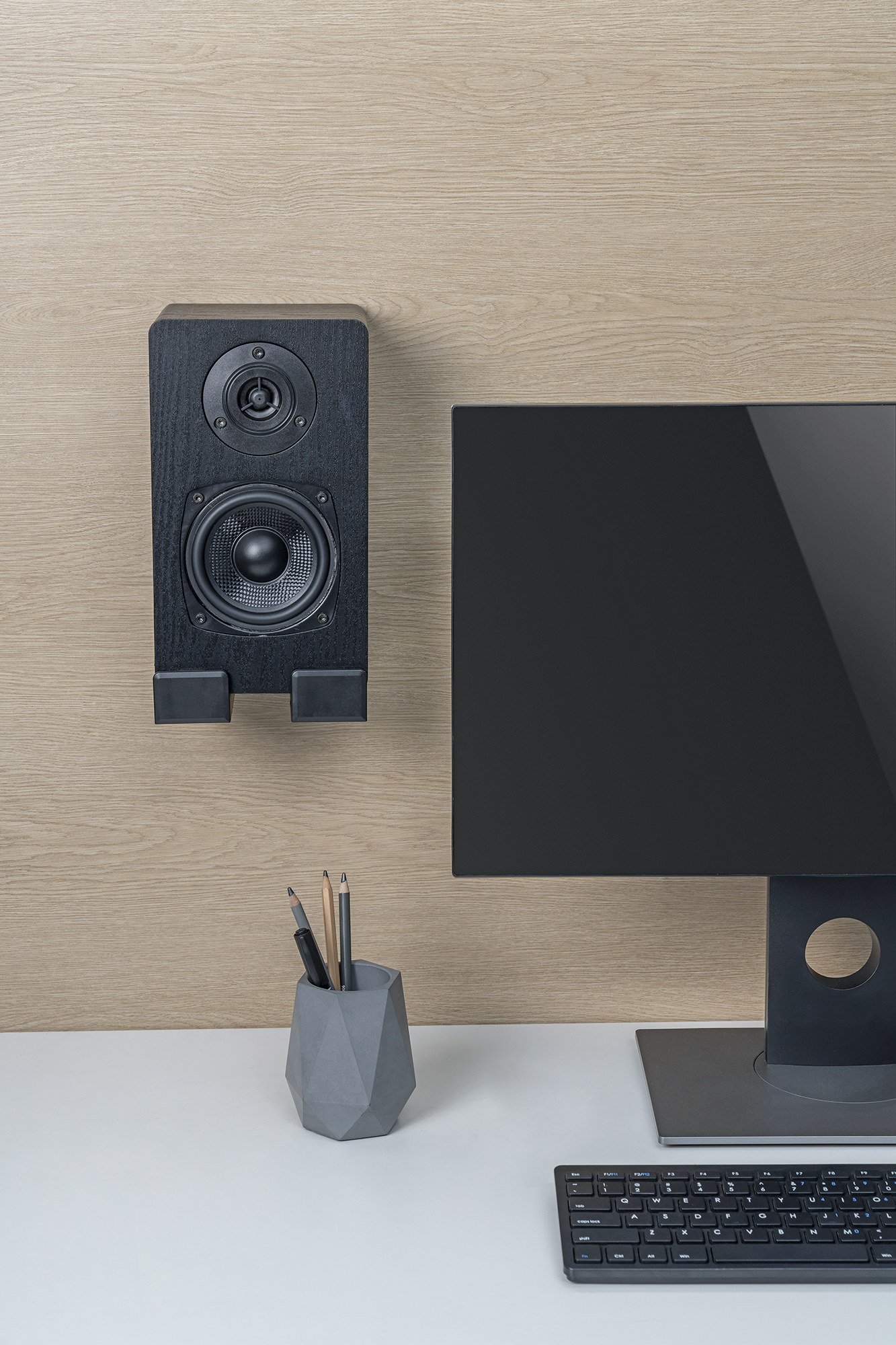 Ein Lautsprecher und ein Computermonitor mit Büromaterial auf einem Schreibtisch. Der Lautsprecher hängt an einer Holzwand.