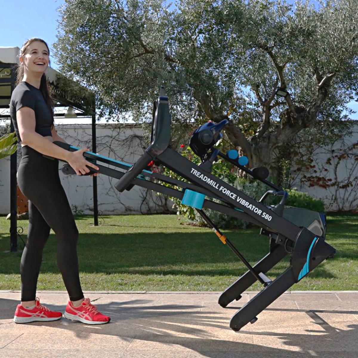 Mujer sosteniendo una cinta de correr. Está en un parque y la cinta está plegada.
