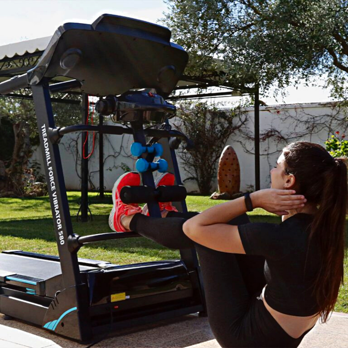 Mujer haciendo abdominales en una cinta de correr. Zapatillas rojas y leggings negros.