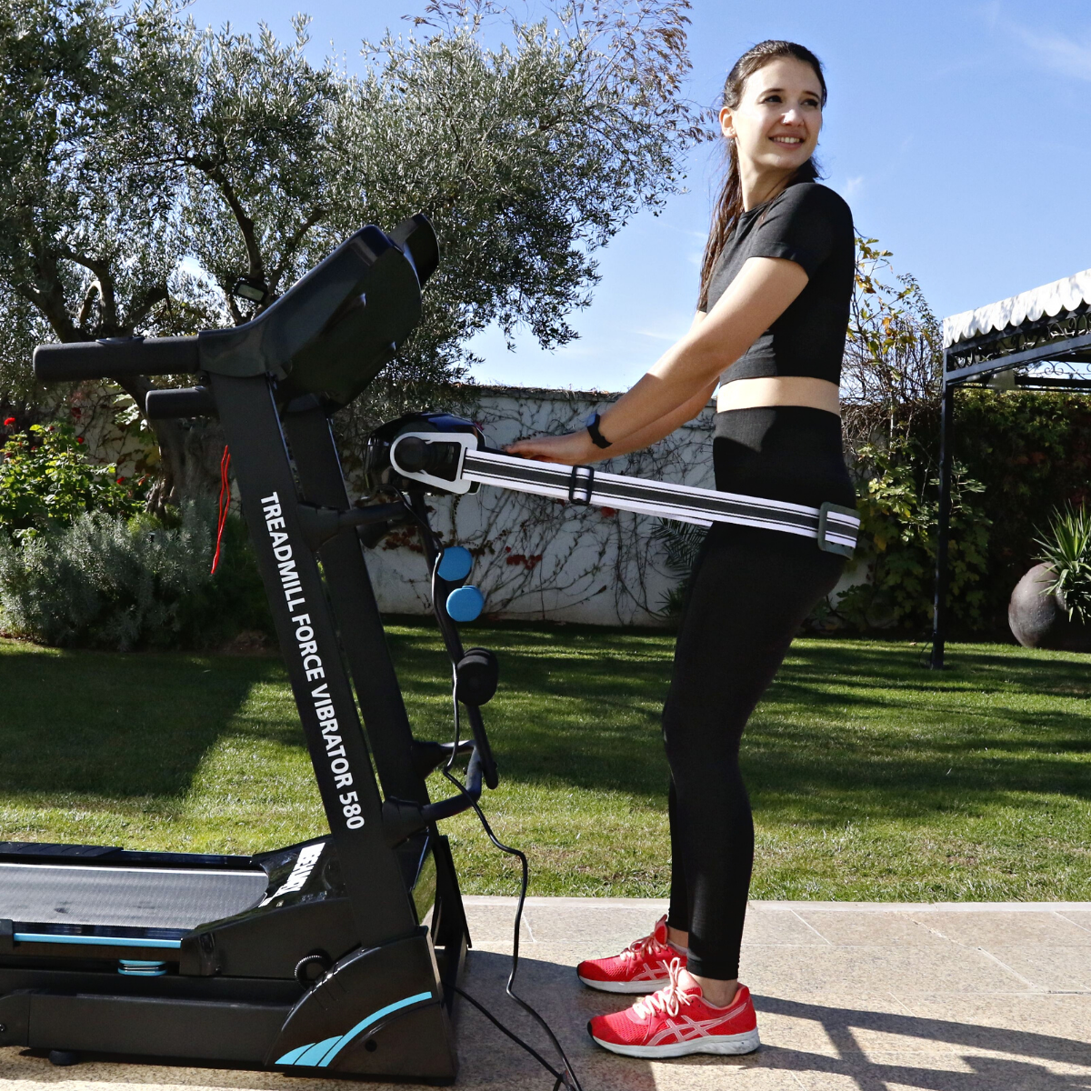 Una mujer haciendo ejercicio en una cinta de correr al aire libre. Está sonriendo y lleva ropa de entrenamiento.