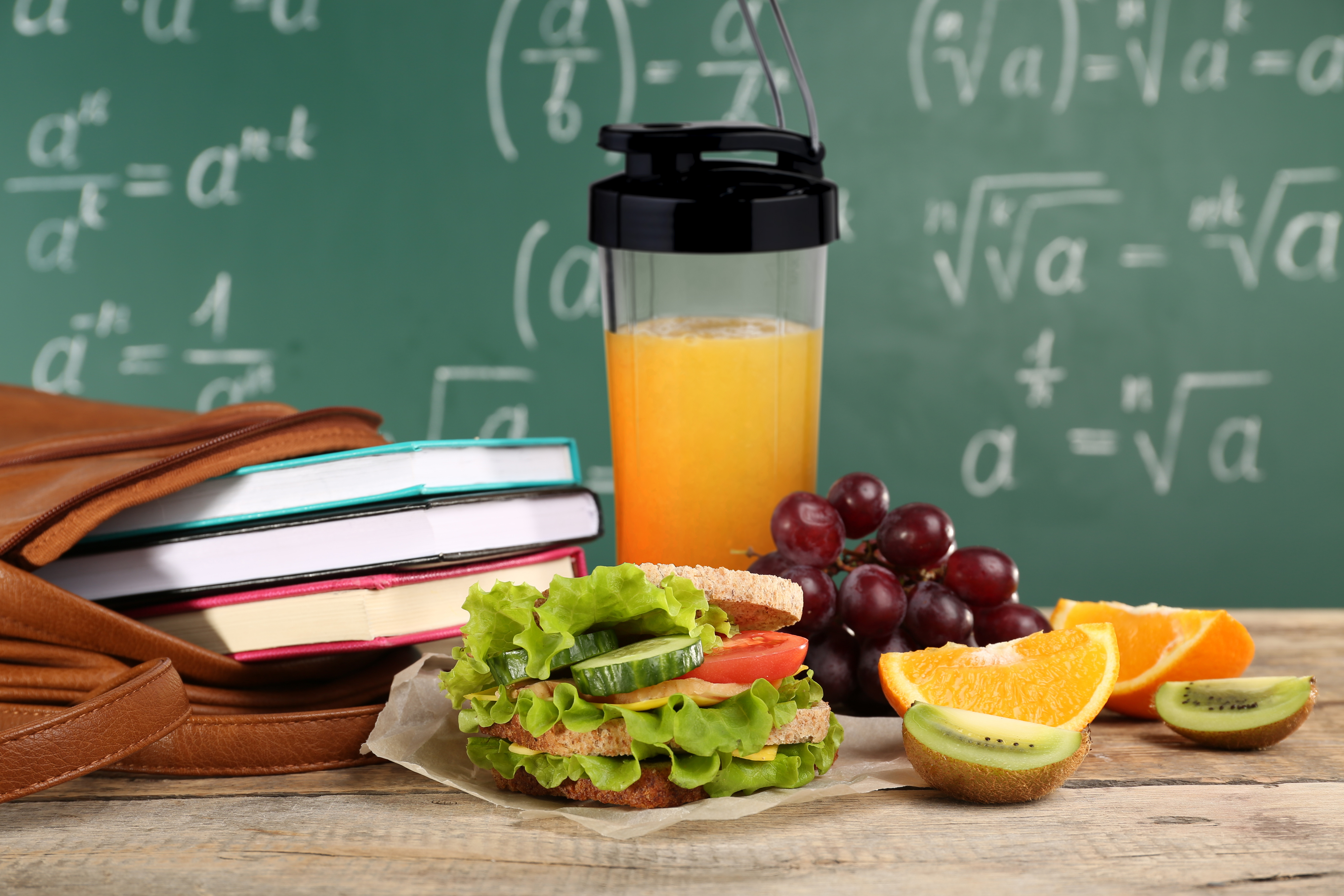 Sandwich, sap en fruit op een houten tafel, met een schoolbord op de achtergrond.