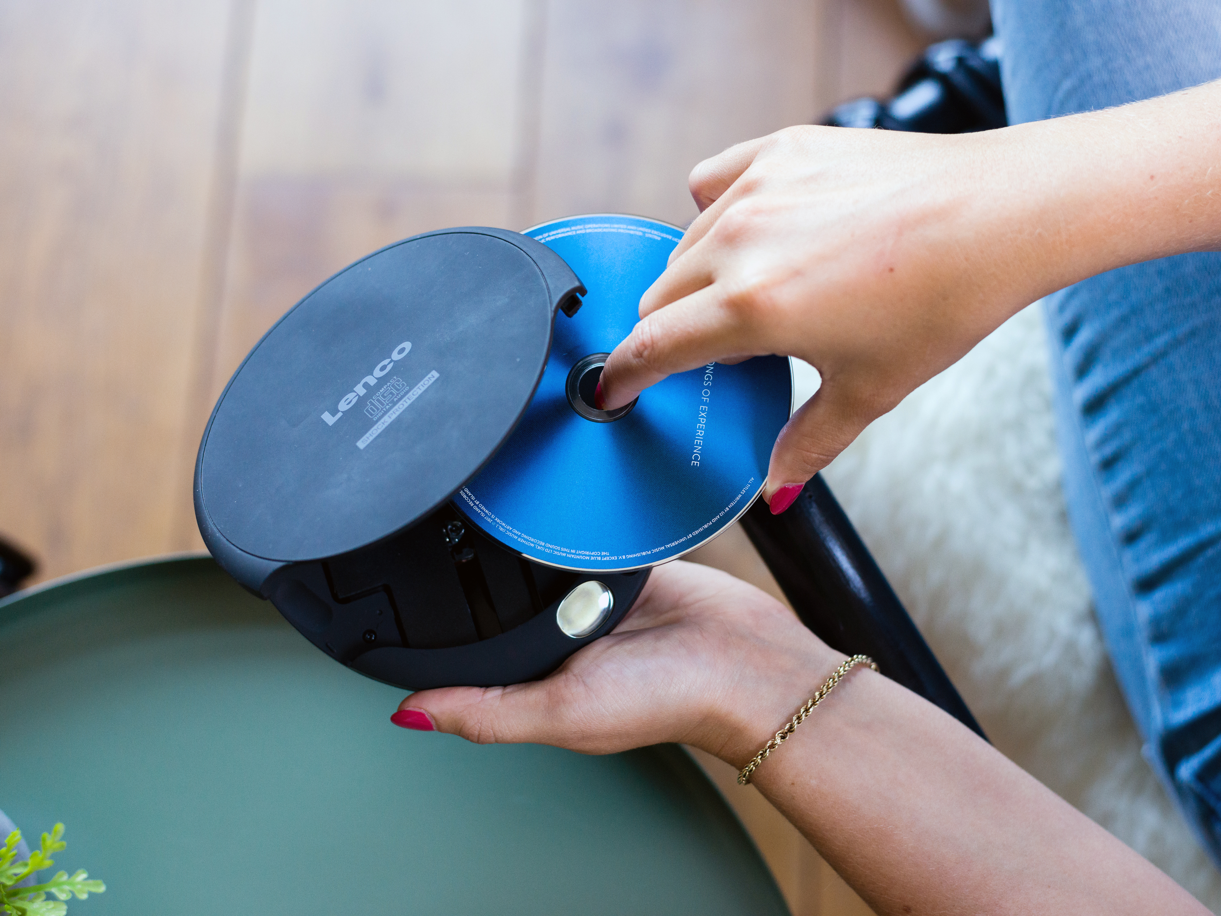 Dłonie wkładające niebieską płytę CD do czarnego przenośnego odtwarzacza CD, na zielonym stole.