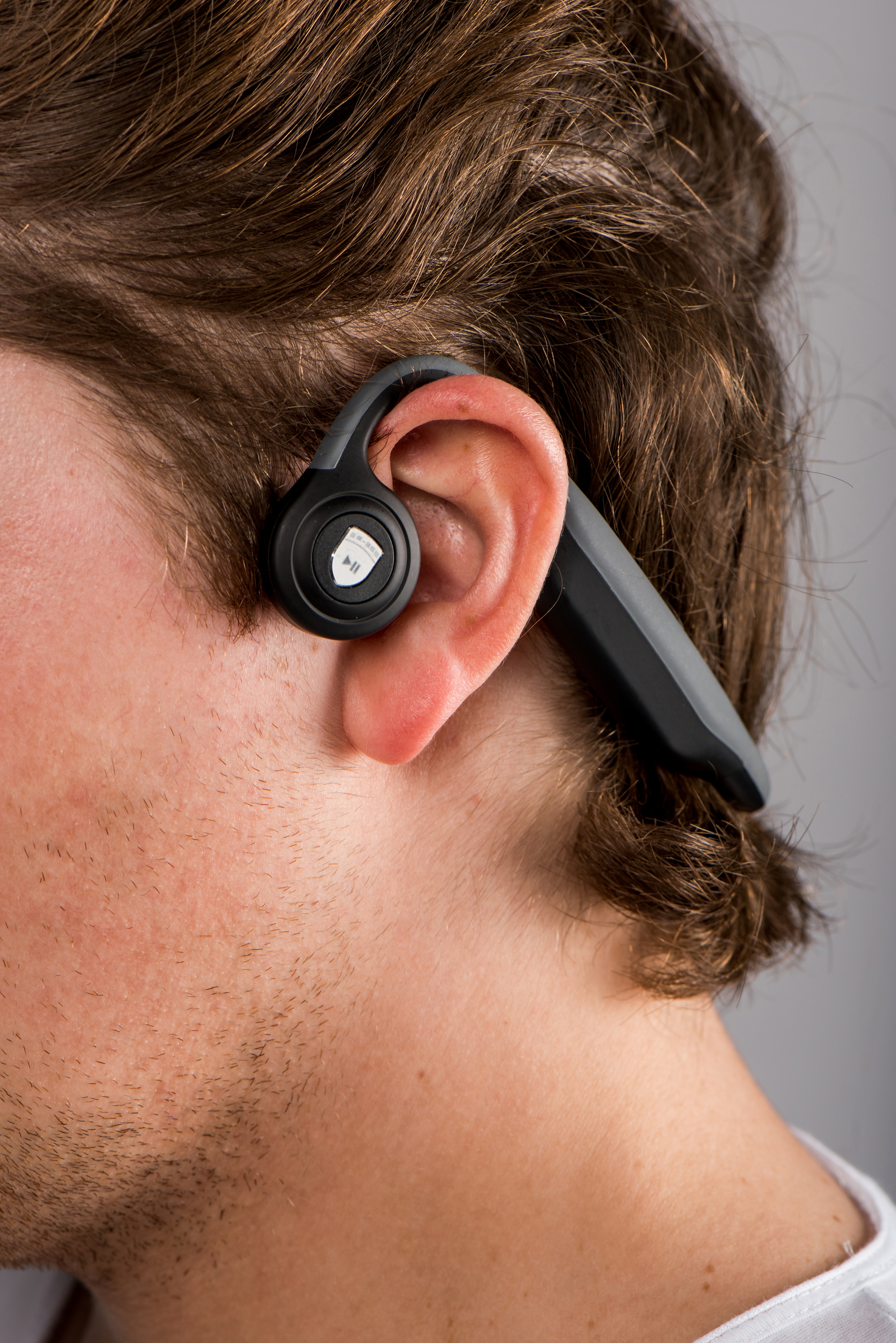 Mężczyzna noszący czarny i szary bezprzewodowy zestaw słuchawkowy w uchu. Szare tło.