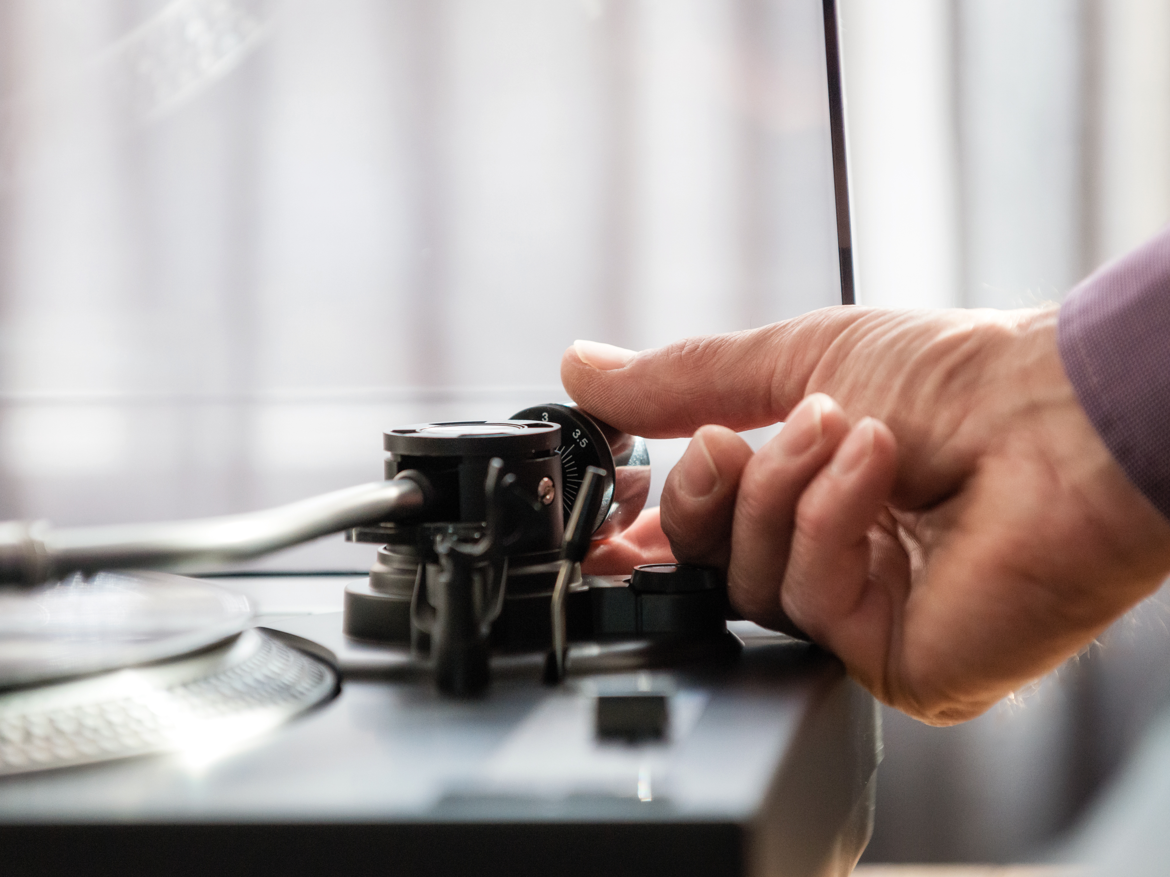 Dłoń regulująca pokrętło na gramofonie, zbliżenie z miękkim skupieniem.