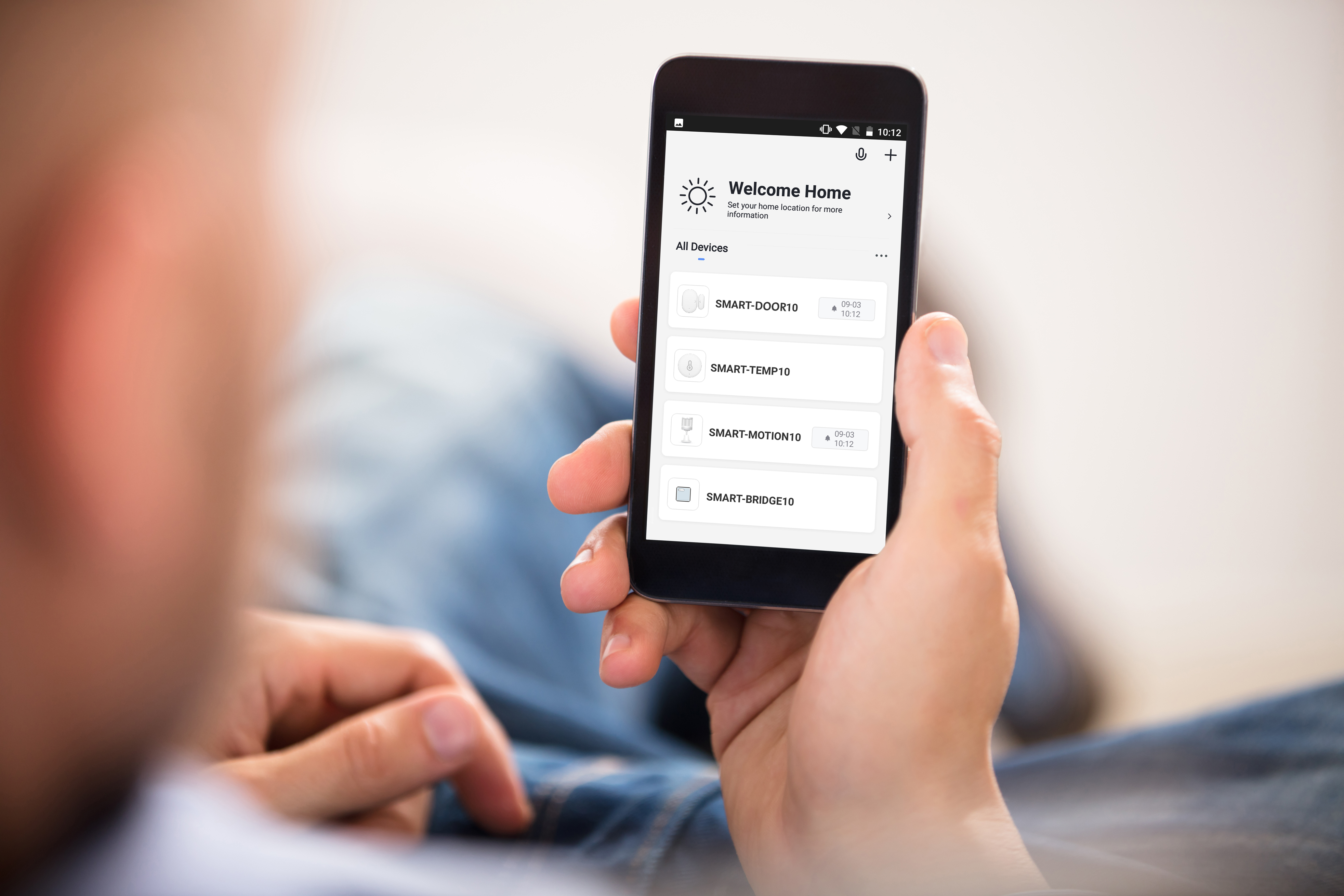 Person hält ein Smartphone mit einer Smart-Home-App-Oberfläche mit Gerätebedienung.