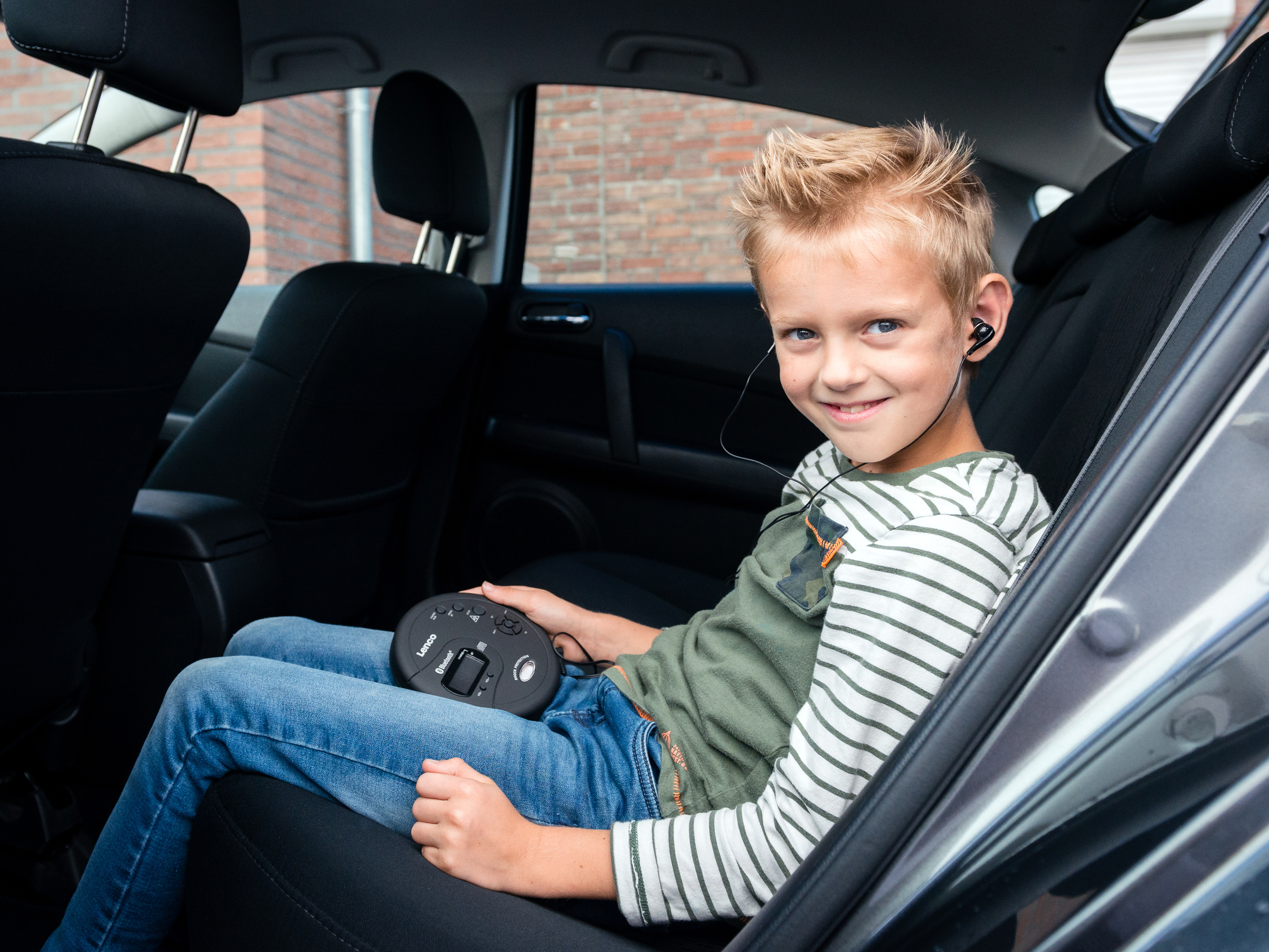 Młody chłopiec w samochodzie w słuchawkach, uśmiechnięty i trzymający przenośny odtwarzacz CD.