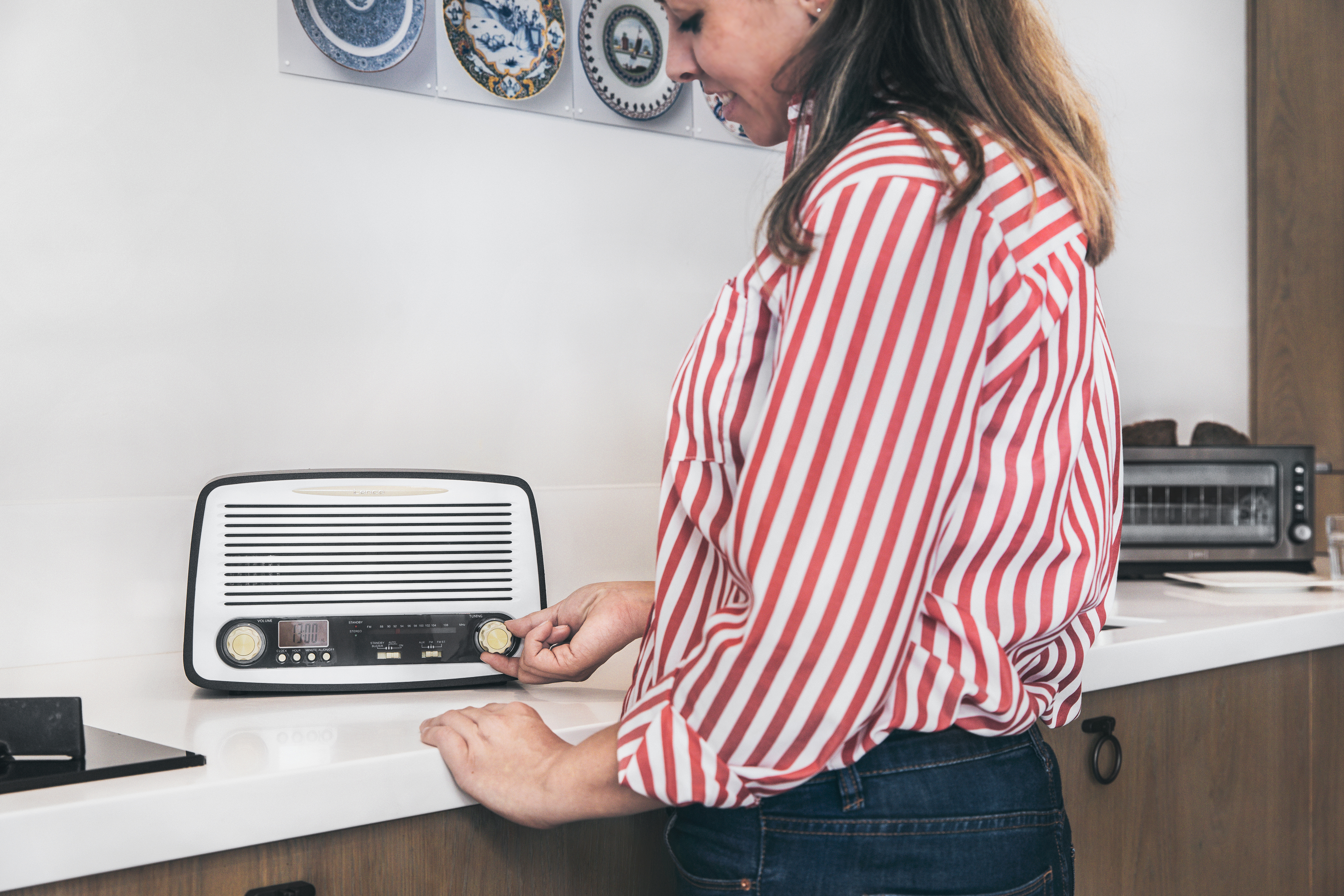 A woman in a red and white striped shirt adjusts a radio on a counter.