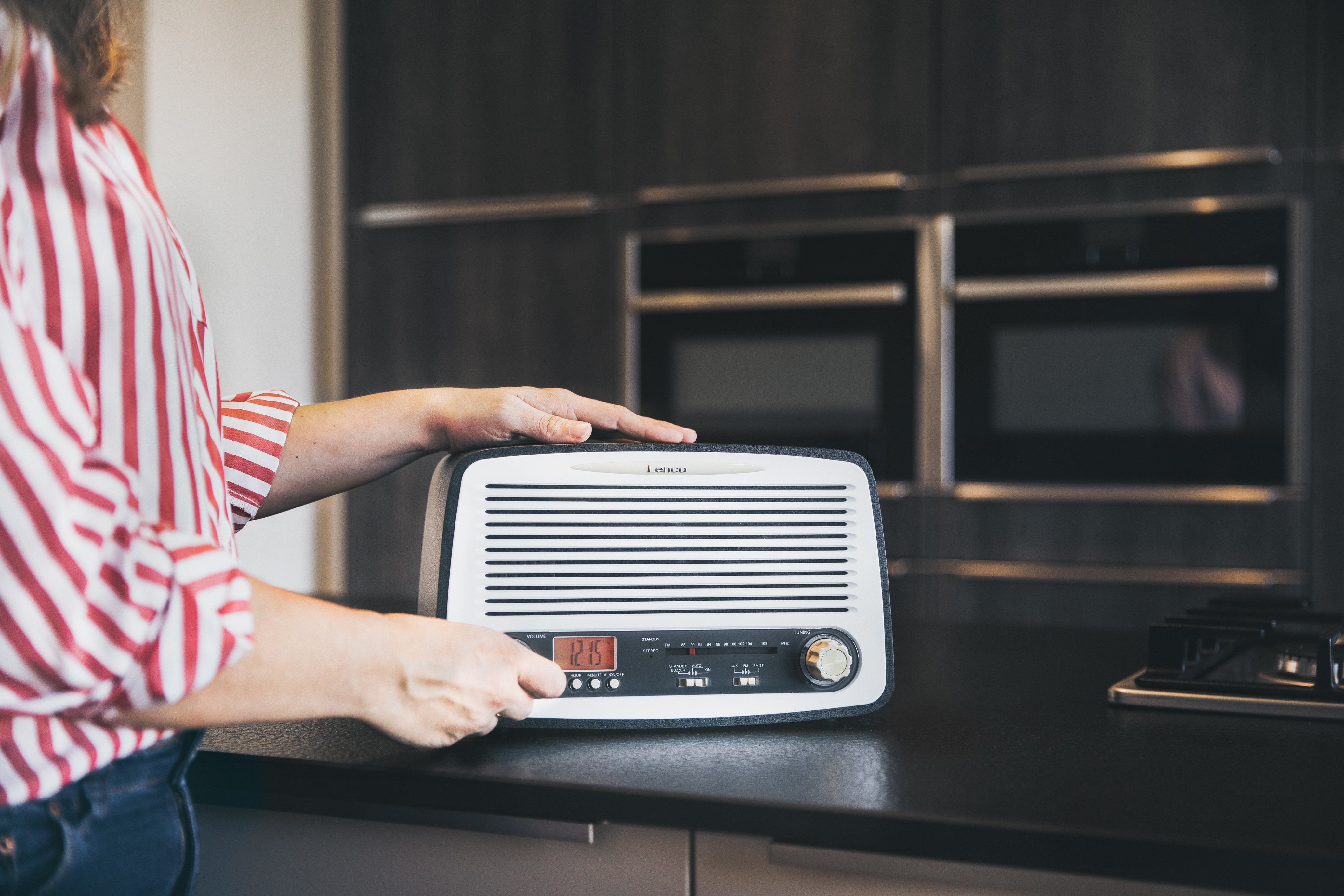 A person's hands adjusting the settings on a retro-style radio with a digital display and knobs.