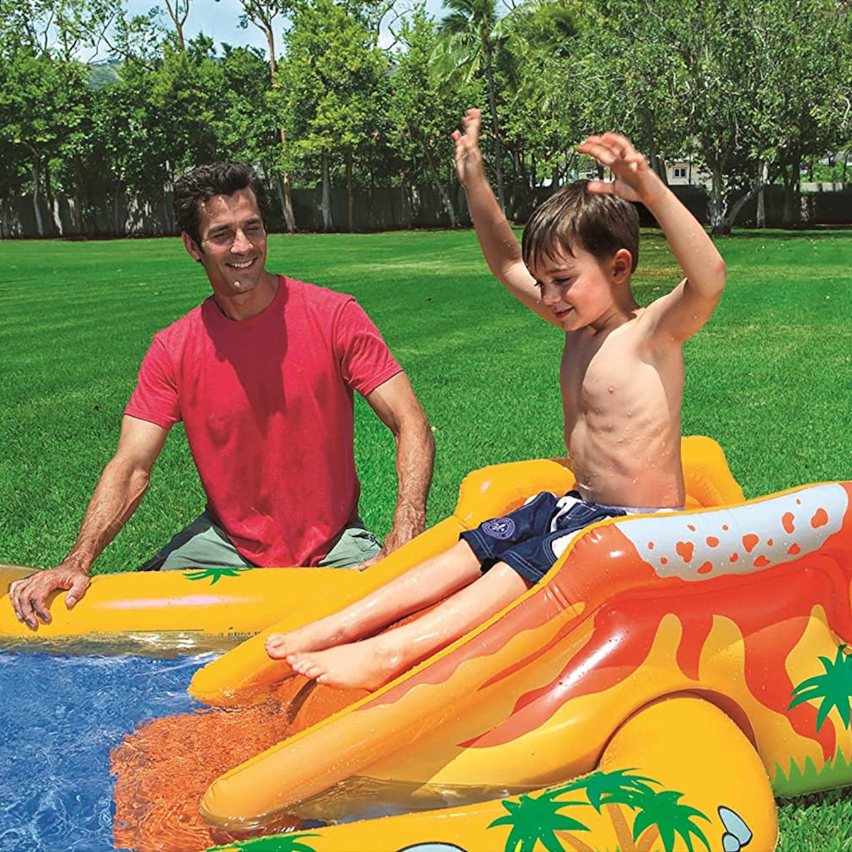 Mężczyzna i dziecko w basenie ze zjeżdżalnią. Dziecko zjeżdża. Mężczyzna siedzi.