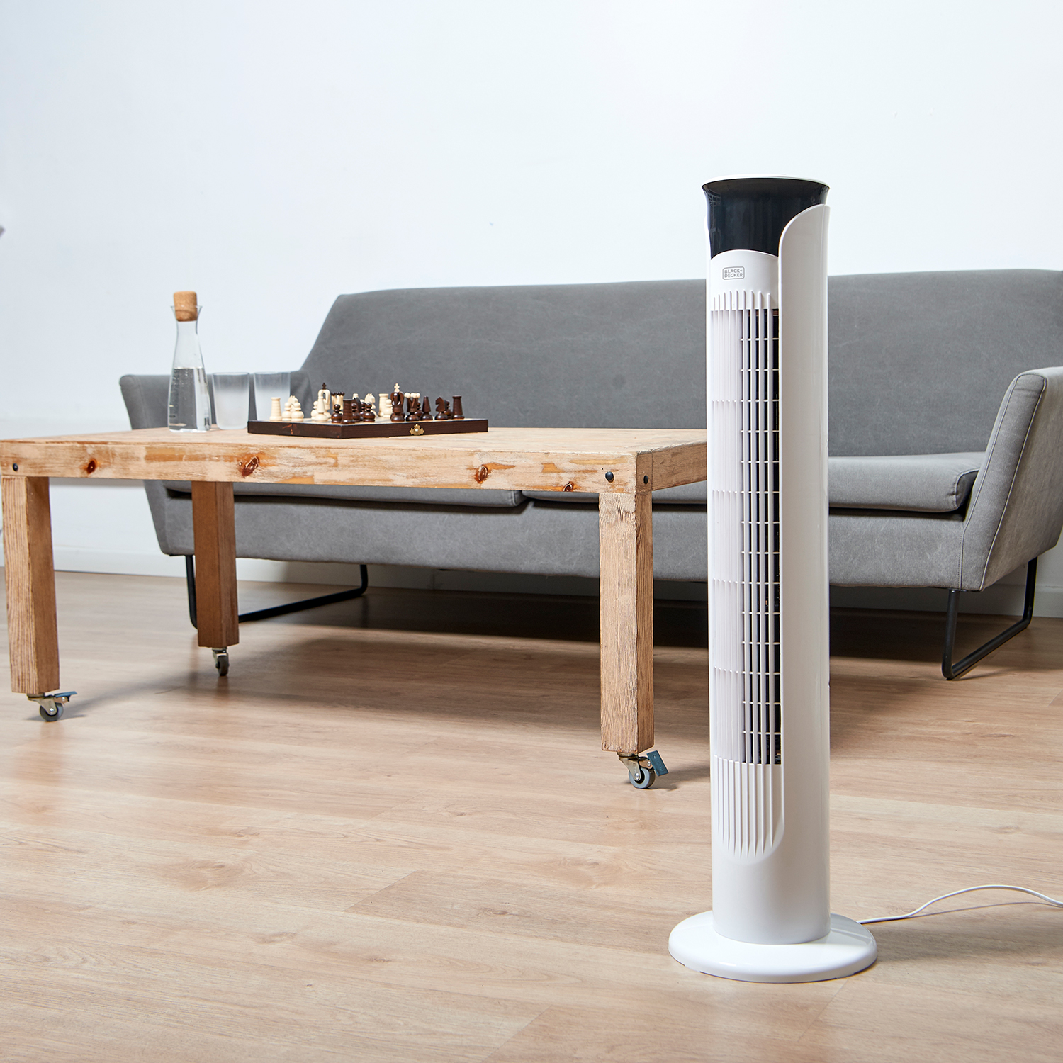 Ein weißer und schwarzer Ventilator steht neben einem Tisch. Ein Schachspiel steht auf dem Tisch.