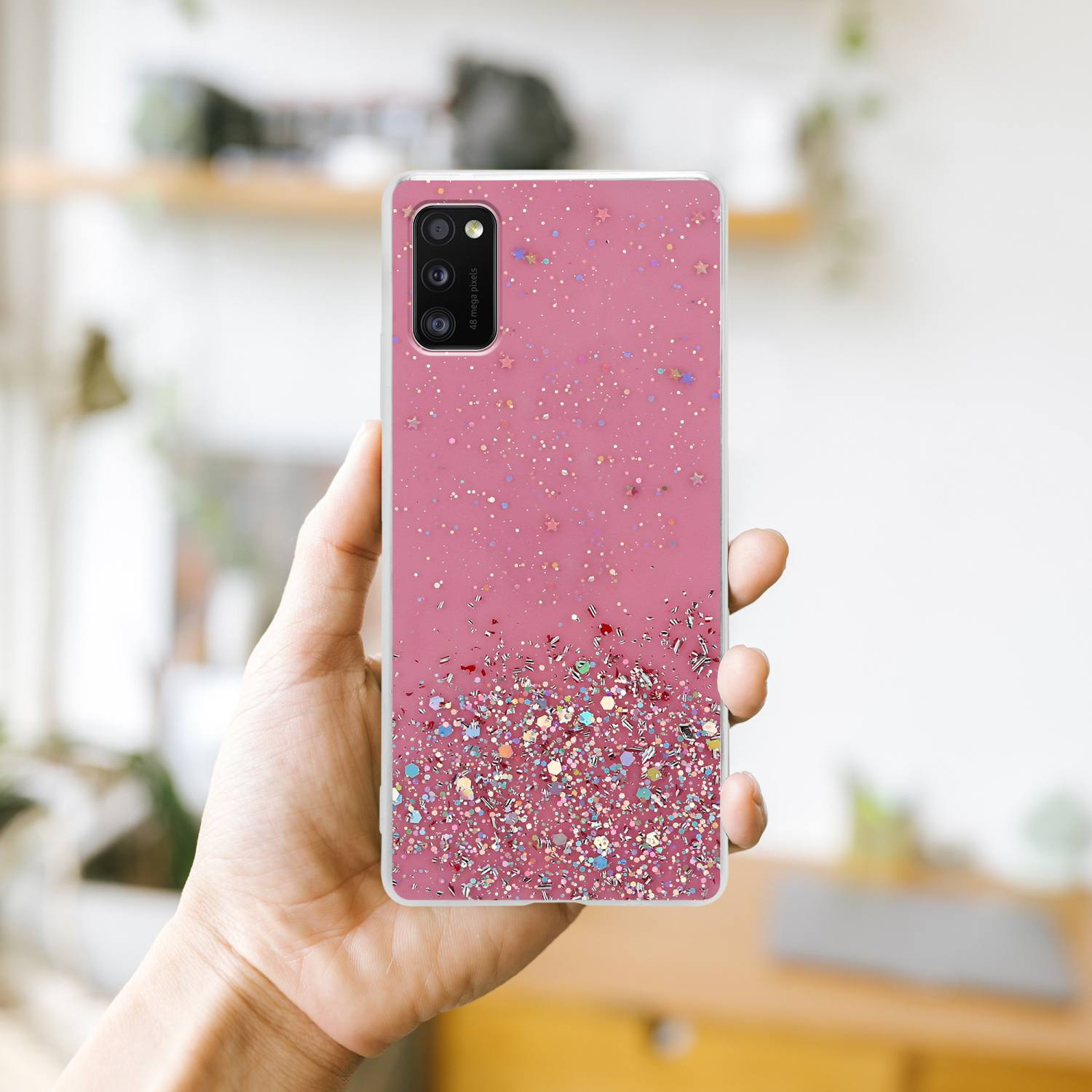 Rosa Handyhülle mit Glitzer auf der Rückseite, in der Hand gehalten. Die Kamera des Telefons ist sichtbar.