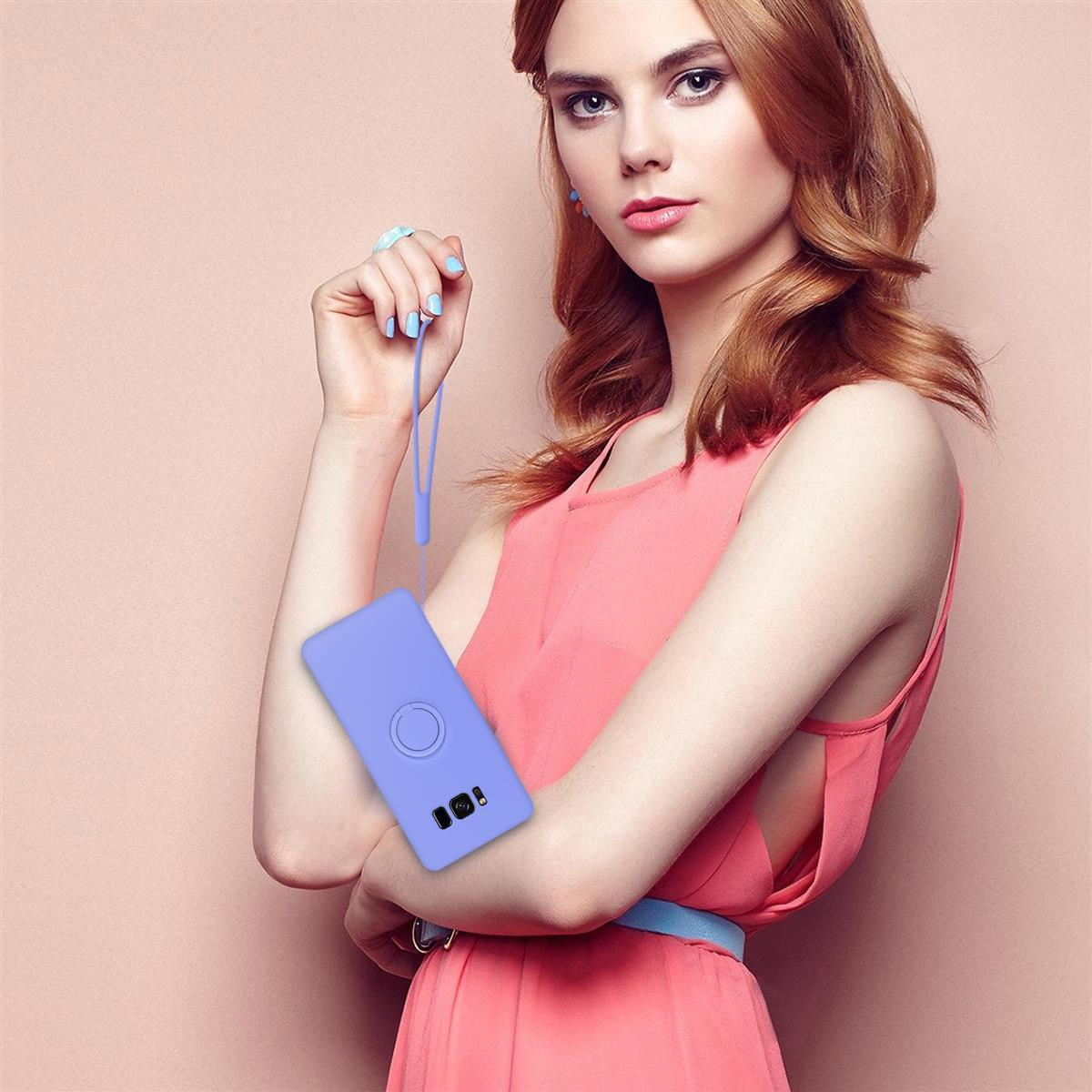 Una donna che tiene un telefono viola chiaro in una custodia, in posa. Sfondo rosa.