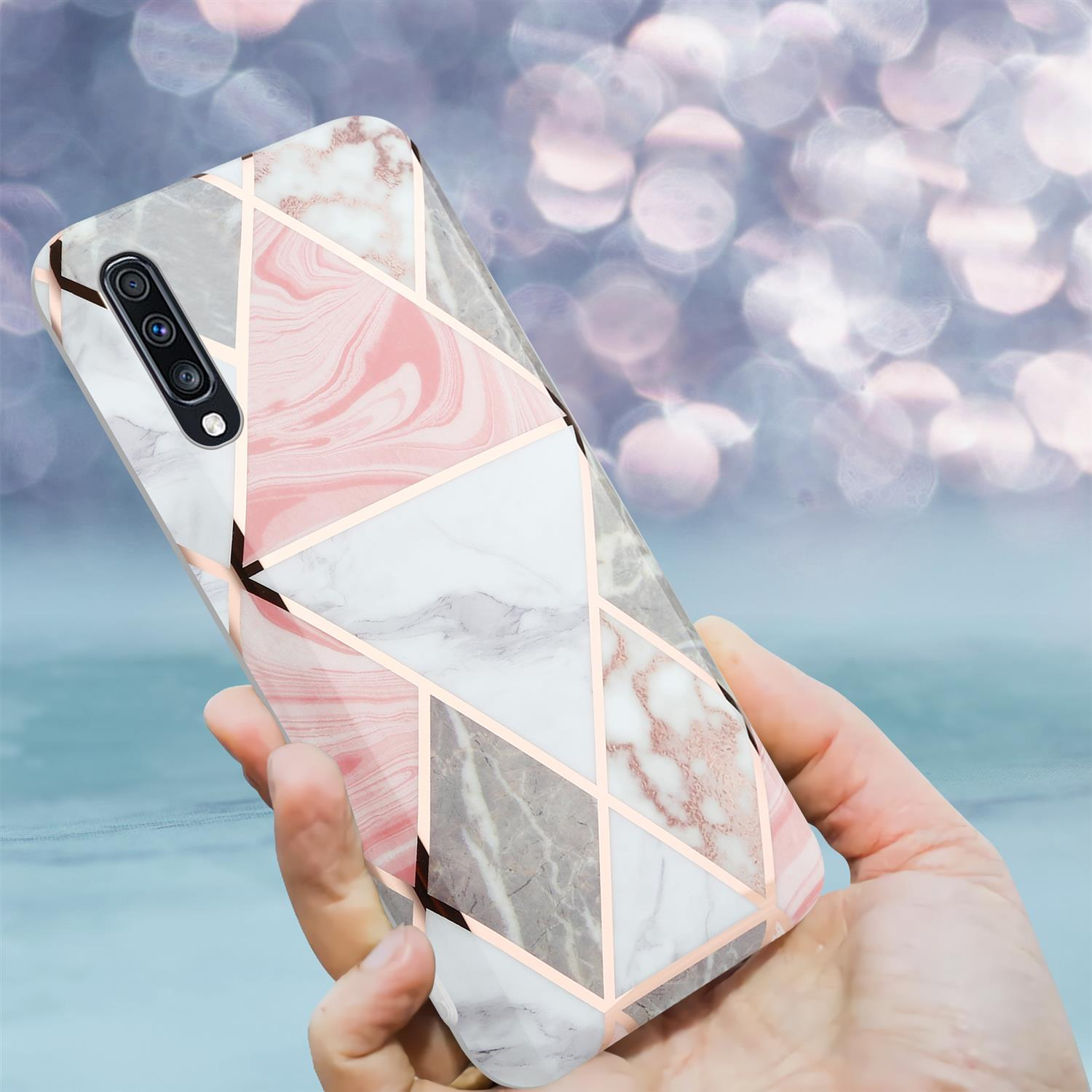 Una mano che tiene una custodia per telefono con un design a marmo e dettagli dorati.