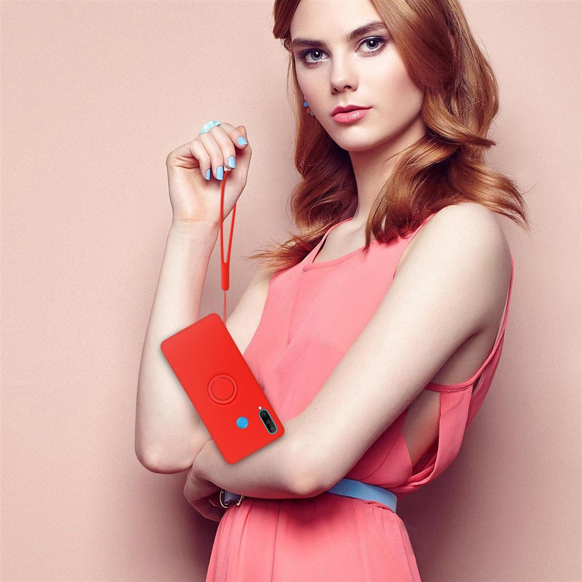 Una donna tiene in mano una custodia rossa con un anello. Indossa un vestito e si trova di fronte a un muro rosa.
