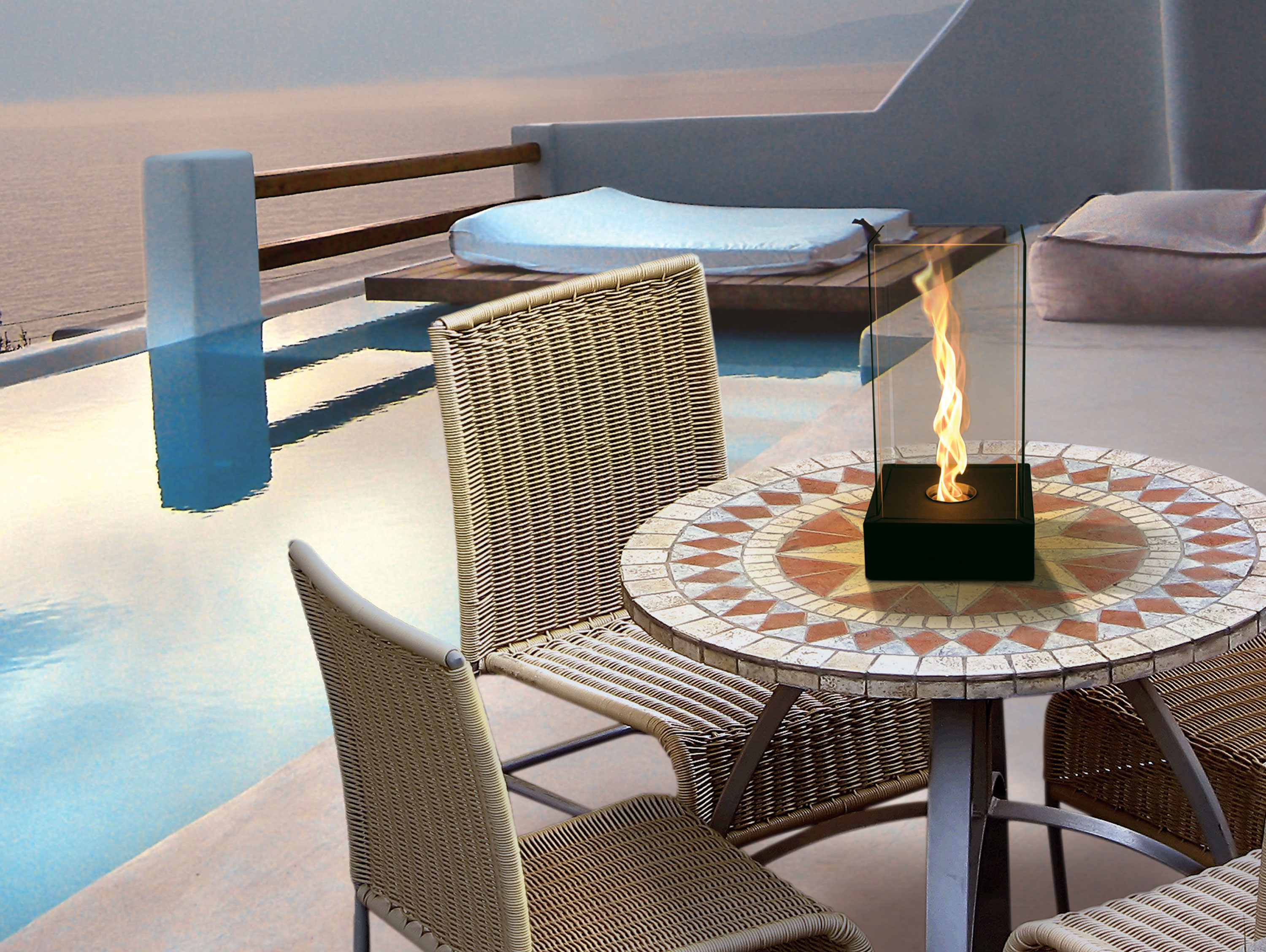 Hoguera en mesa de mosaico en patio con vista al agua. Dos sillas visibles.