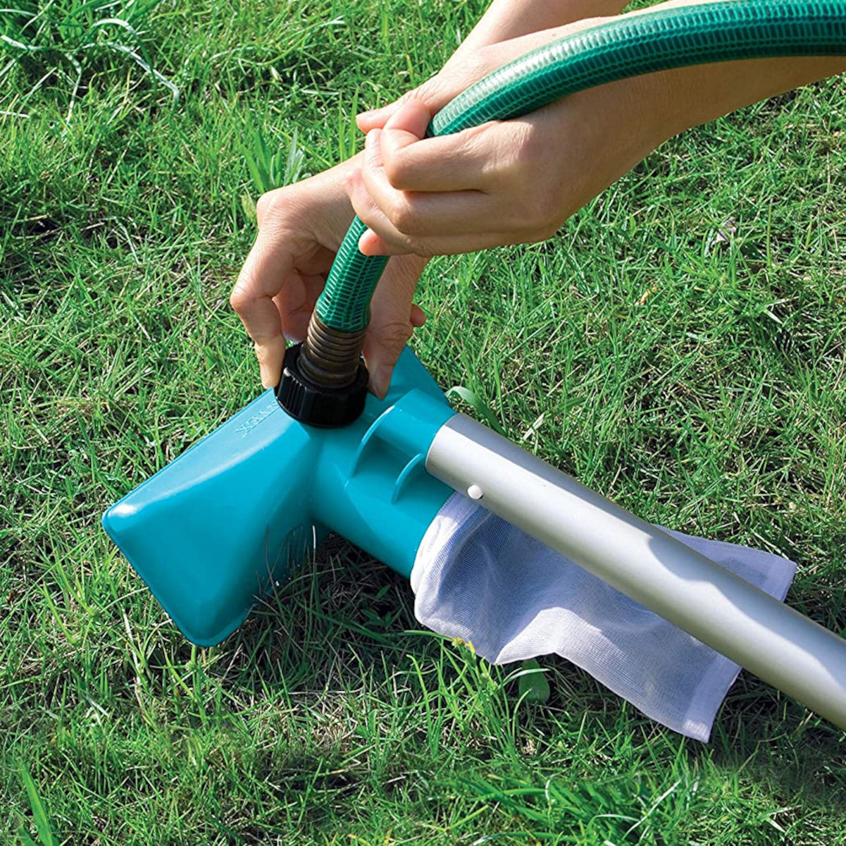 Eine Person verbindet einen grünen Schlauch mit einem blauen Poolstaubsauger auf grünem Gras.