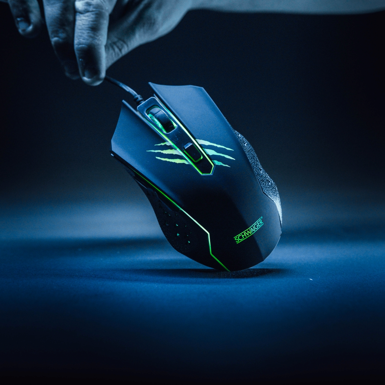 Schwarze Gaming-Maus, Hand hält sie. Die Maus hat grüne Akzente und Krallenspuren.
