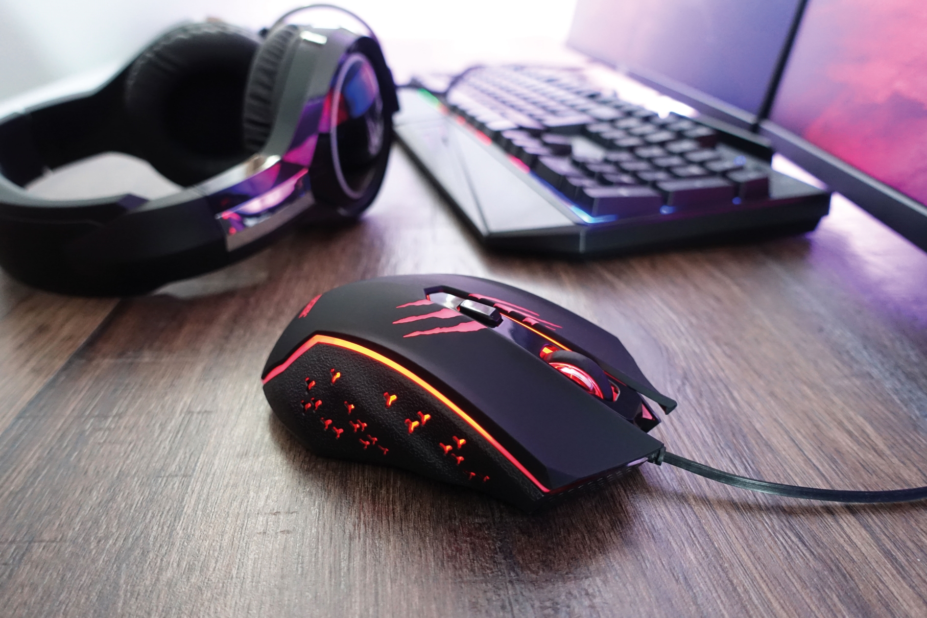 Eine schwarze Gaming-Maus mit roten Akzenten und einem angeschlossenen Kabel auf einer Holzoberfläche.