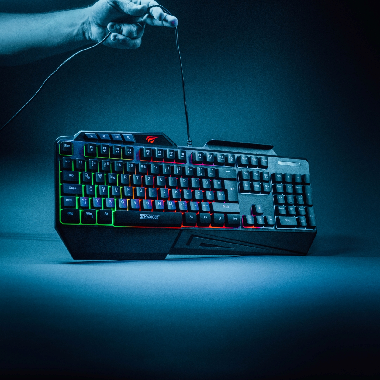 Eine schwarze Gaming-Tastatur mit leuchtenden Tasten wird von einer Hand mit Kabel gehalten.