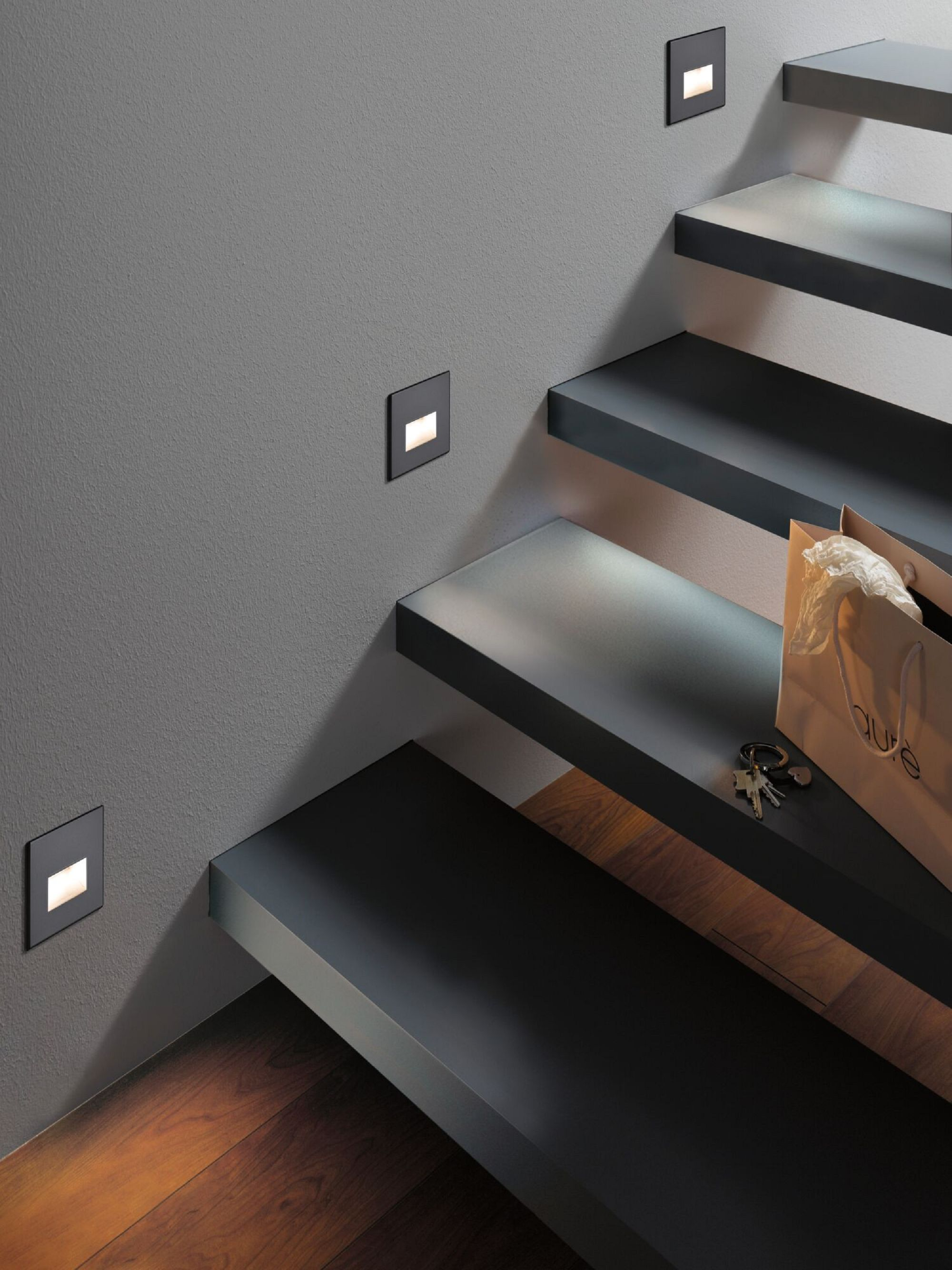 Schody z wpuszczonymi światłami. Światła są kwadratowe i świecą. Papierowa torba i klucze na schodach.