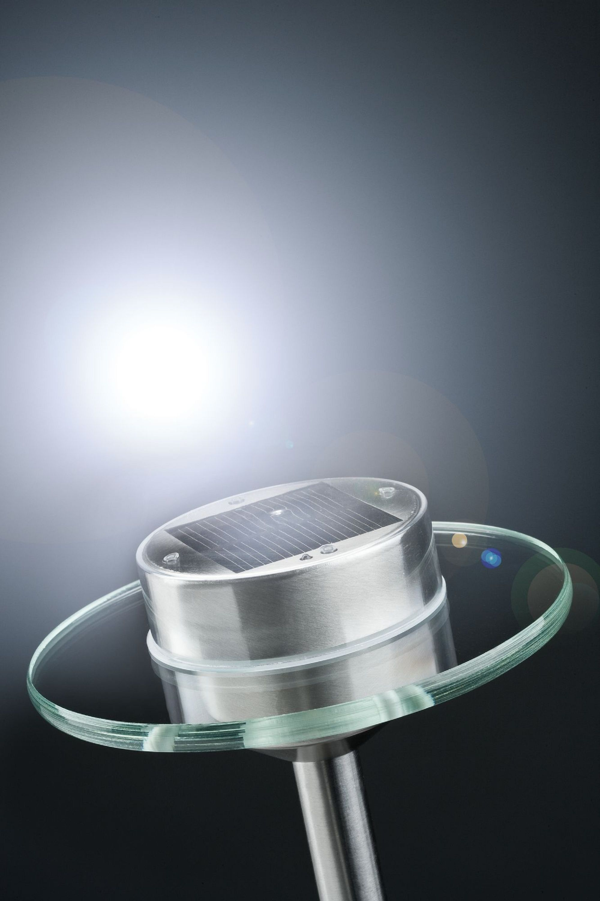 Solarna lampa ogrodowa ze srebrną górą, szklanym pierścieniem i ciemnym tłem.