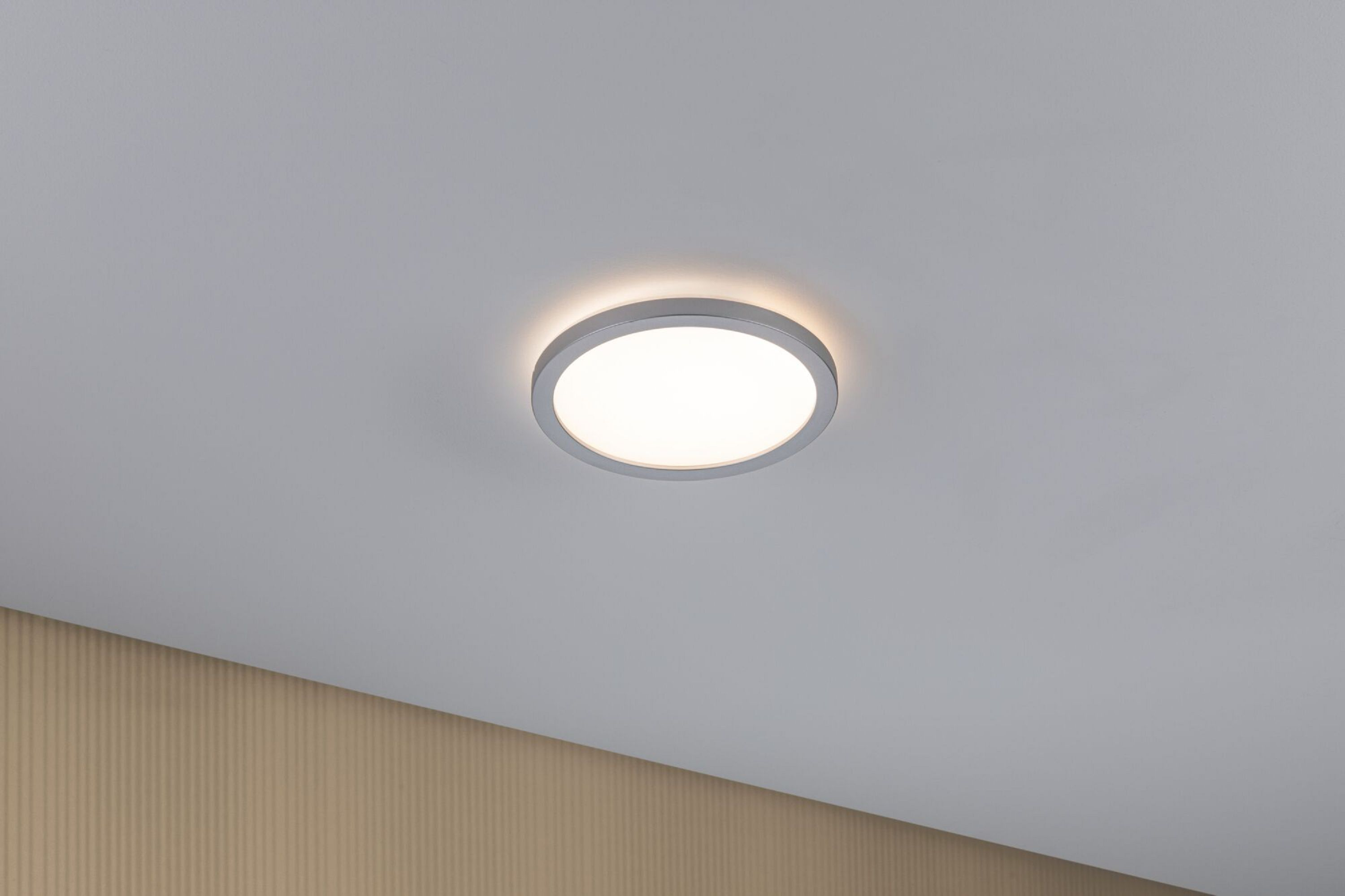 Okrągła, srebrna lampa sufitowa LED, białe światło na białym suficie.