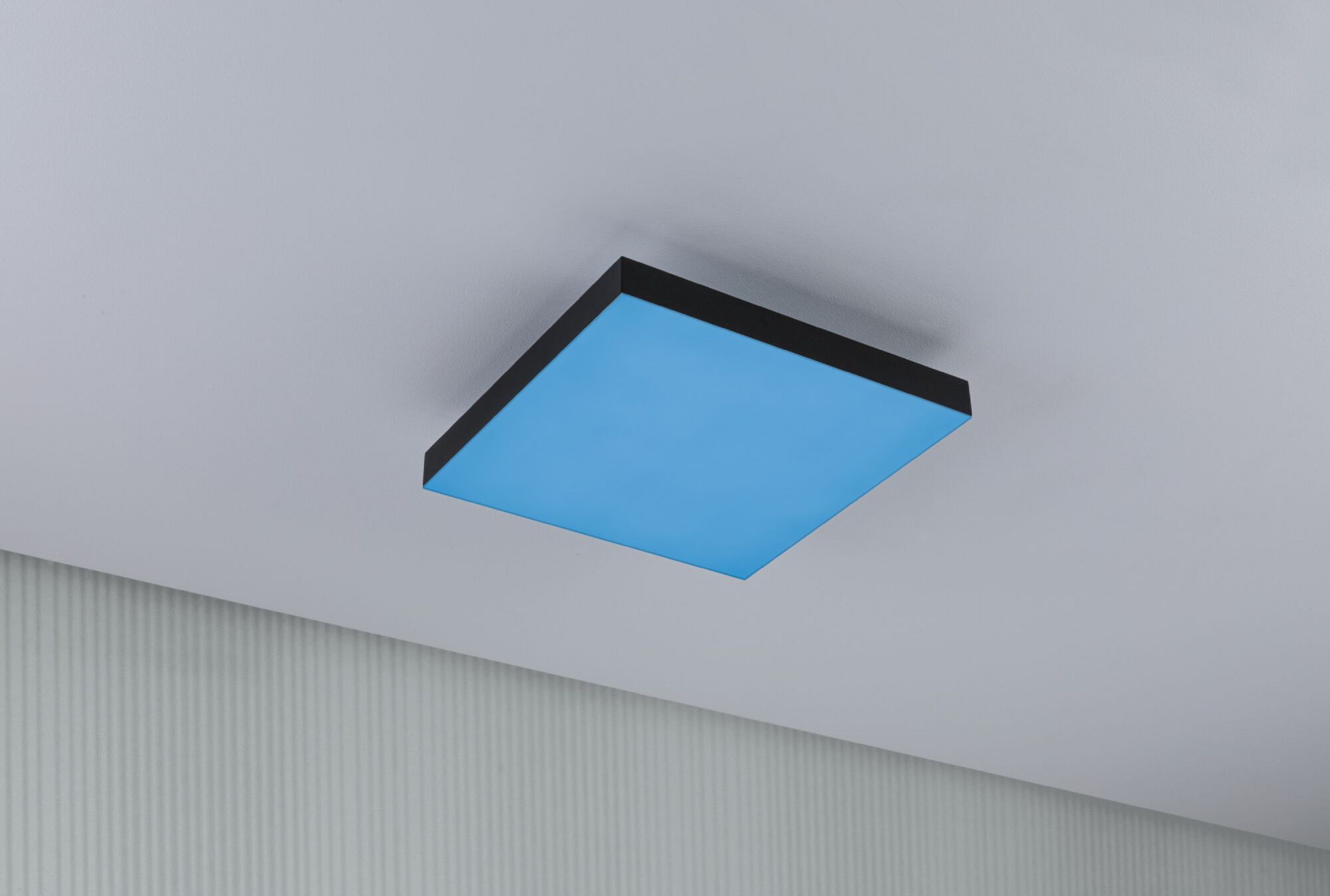 Kwadratowa, niebieska oprawa oświetleniowa z czarną ramą zamontowana na suficie.