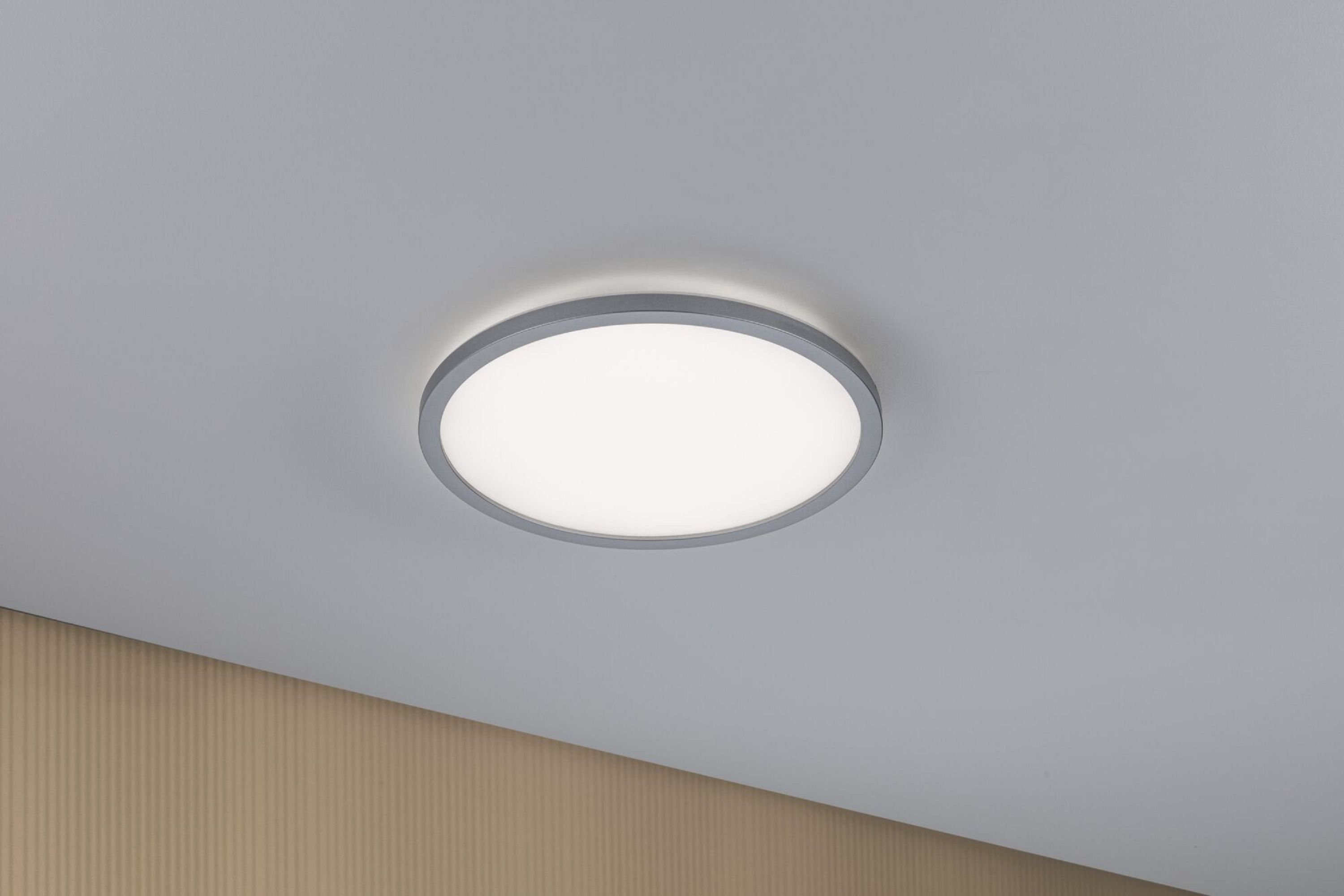Un apparecchio di illuminazione a soffitto rotondo, bianco e argento, montato su un soffitto bianco. La luce è accesa.