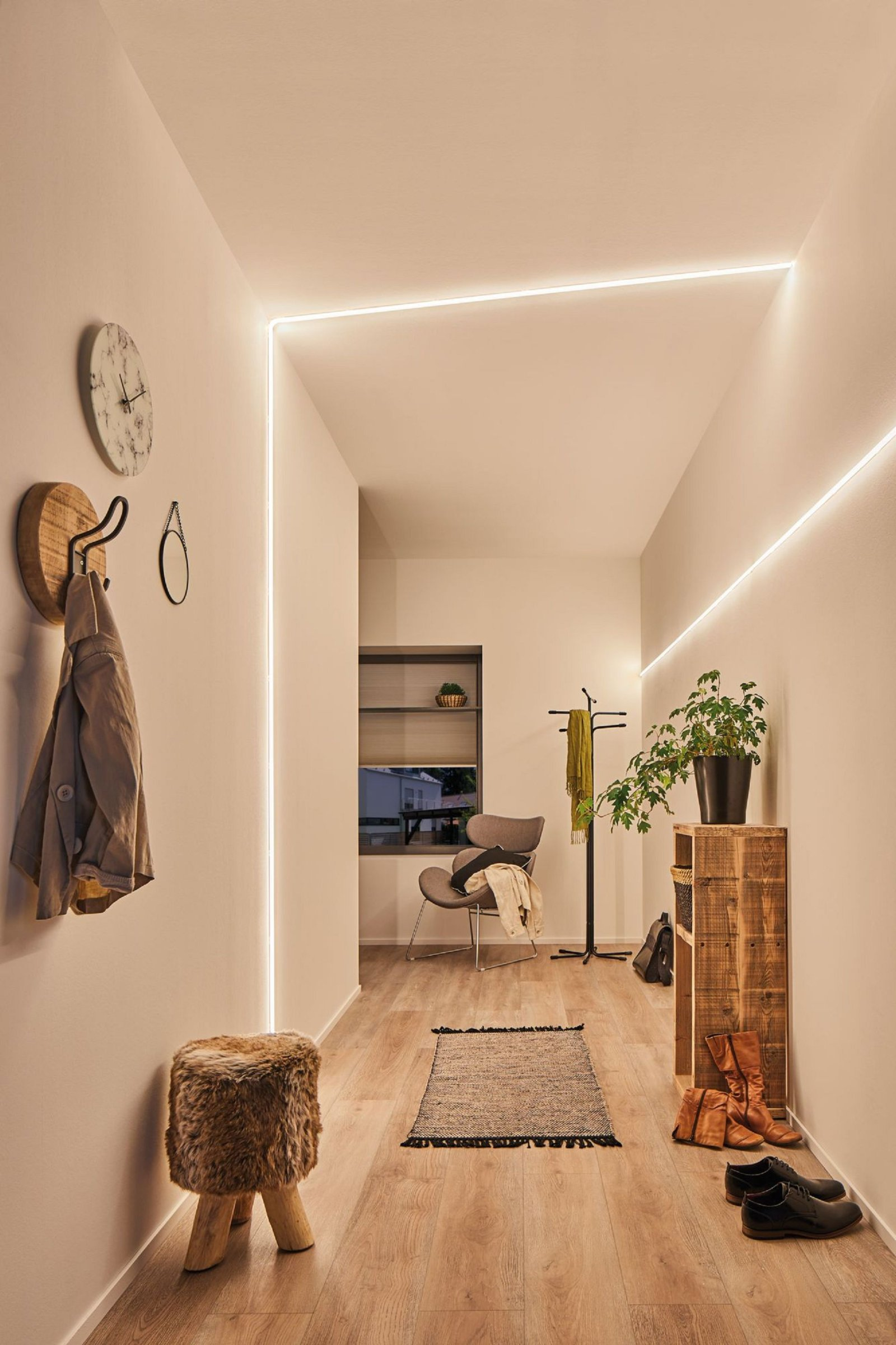 Ein Flur mit Holzboden und dekorativer Wandbeleuchtung. Teppich, Hocker und Kunst sichtbar.