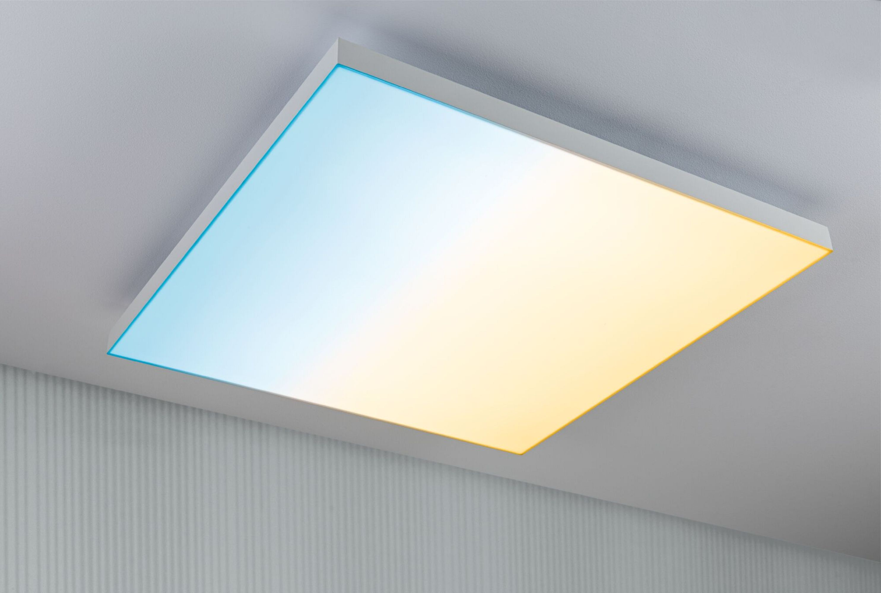 Kwadratowa lampa sufitowa, biała rama z niebiesko-żółtym światłem gradientowym. Zamontowana na teksturowanym białym suficie.