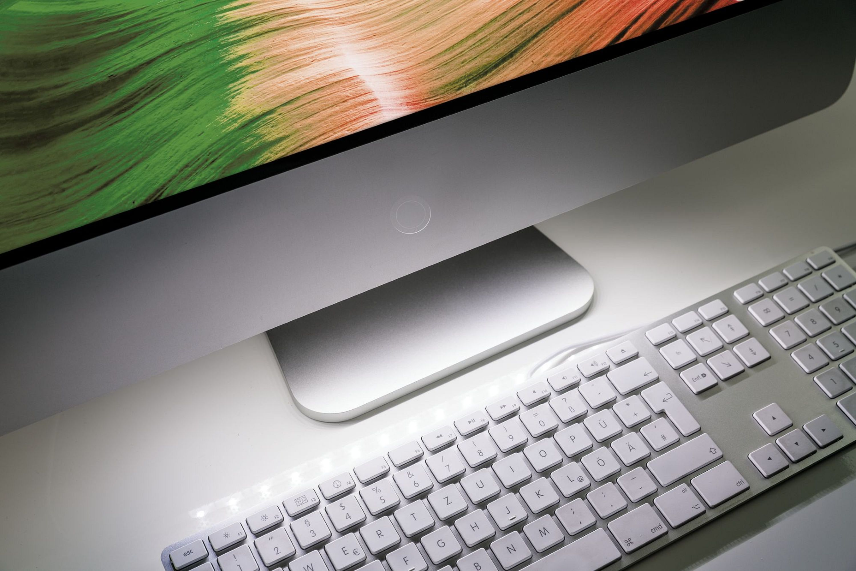 Computer desktop con tastiera. Lo schermo mostra un'immagine colorata, scrivania bianca.