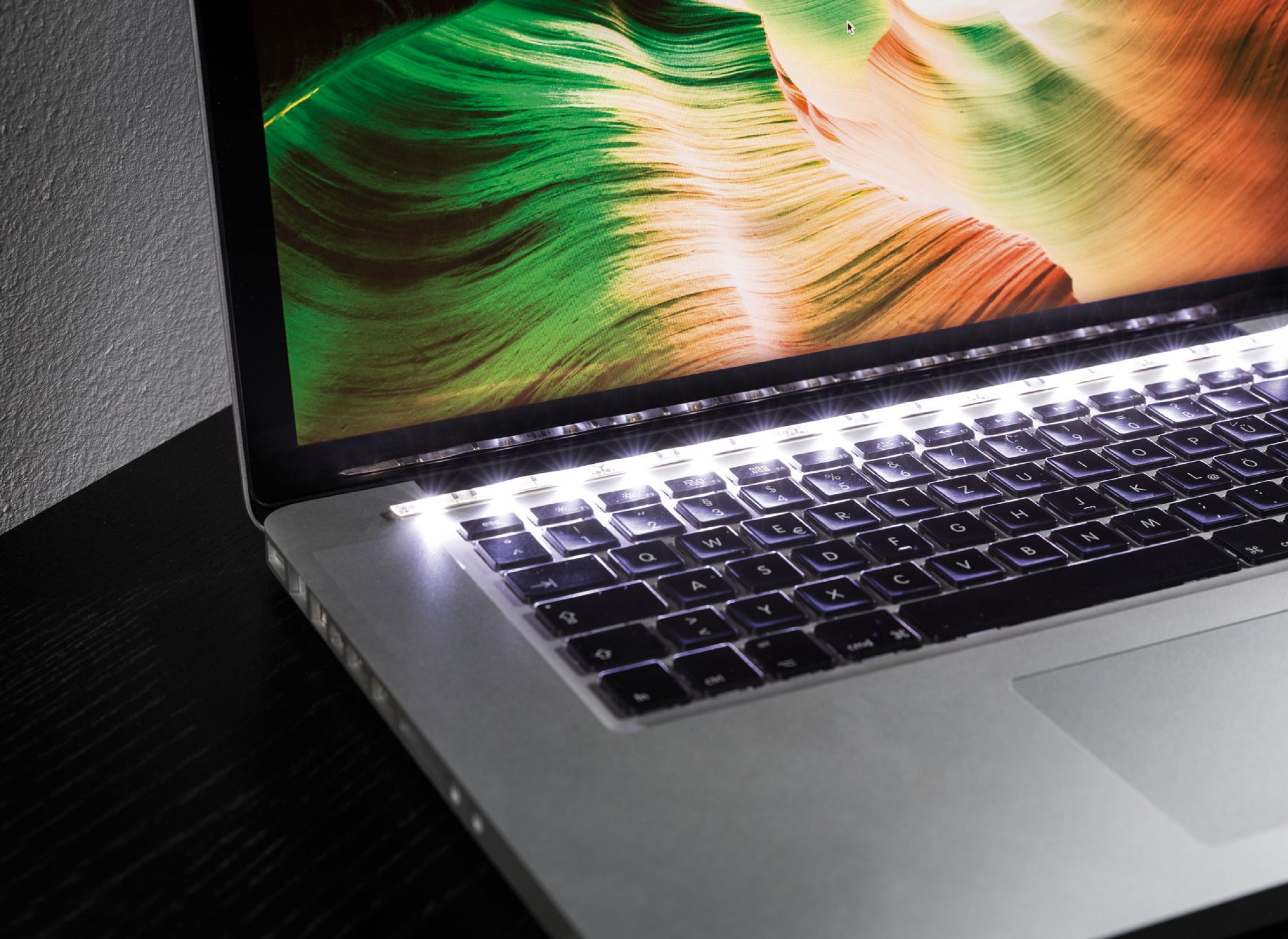 Una tastiera del laptop illuminata da luci LED bianche e luminose lungo i bordi e uno sfondo colorato.
