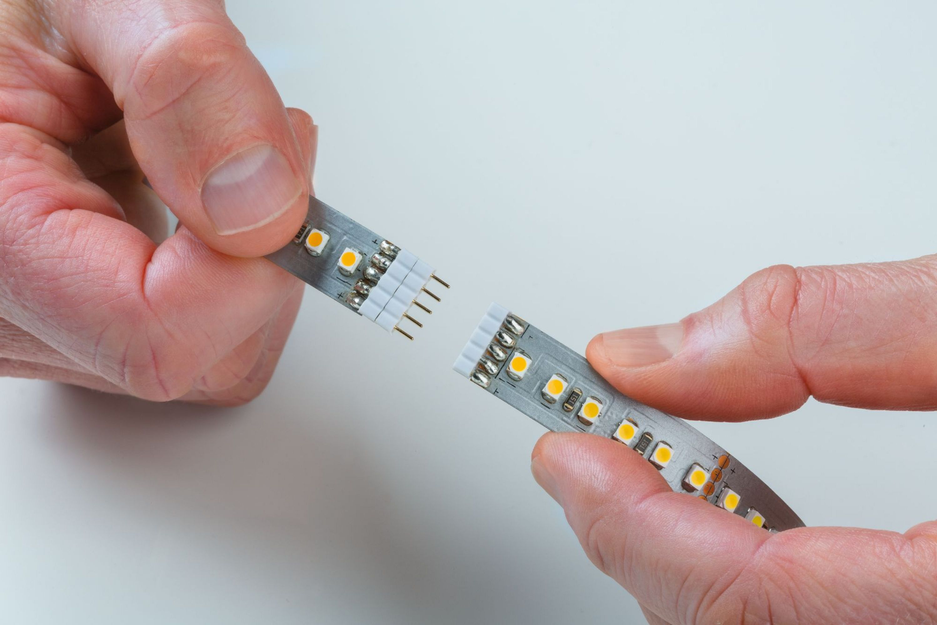 Dwie ręce trzymające paski LED, przygotowujące się do ich połączenia. Białe tło.