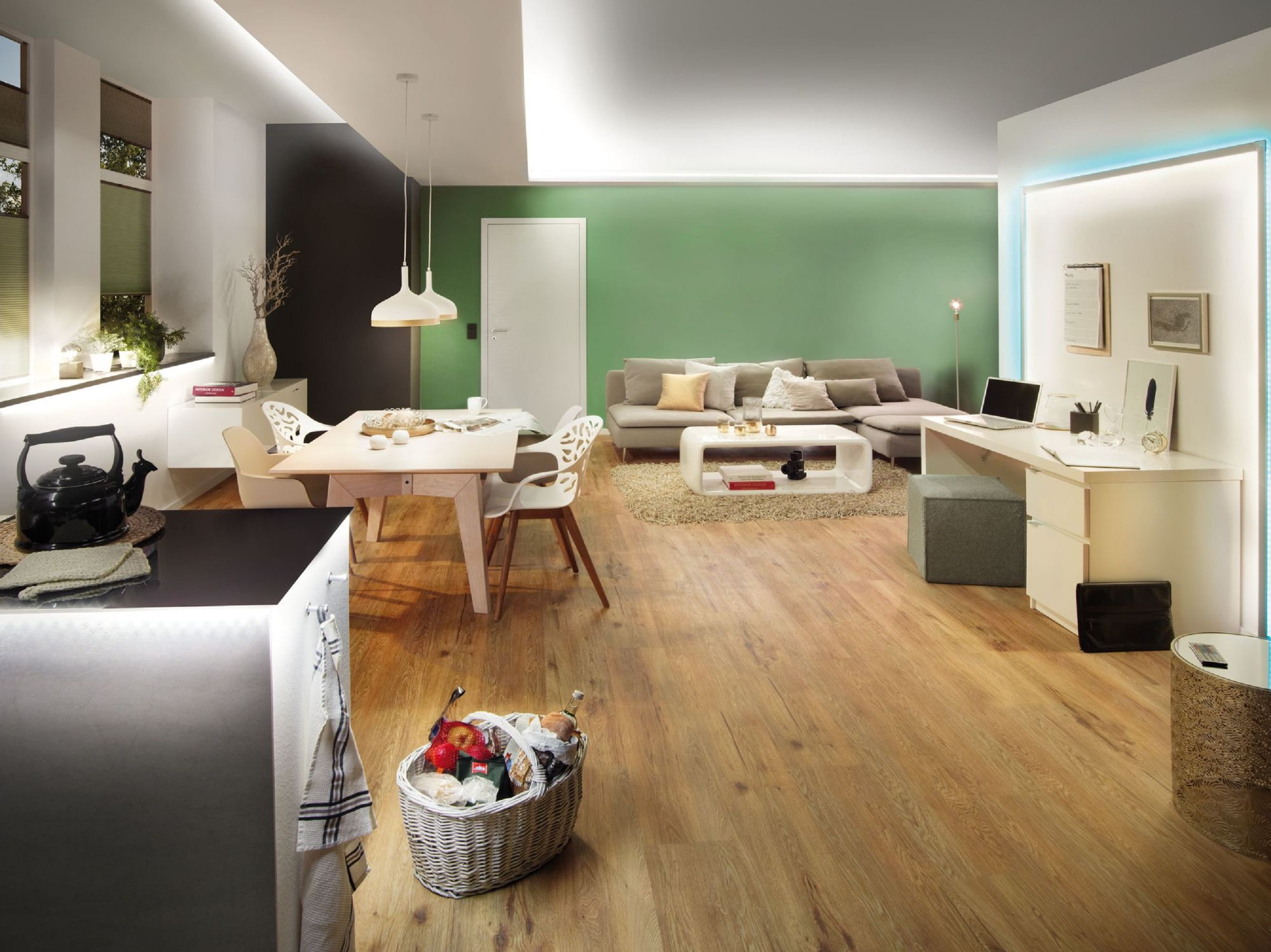 Salon z jasną drewnianą podłogą. Zielona ściana i sofa. Kosz z jedzeniem.