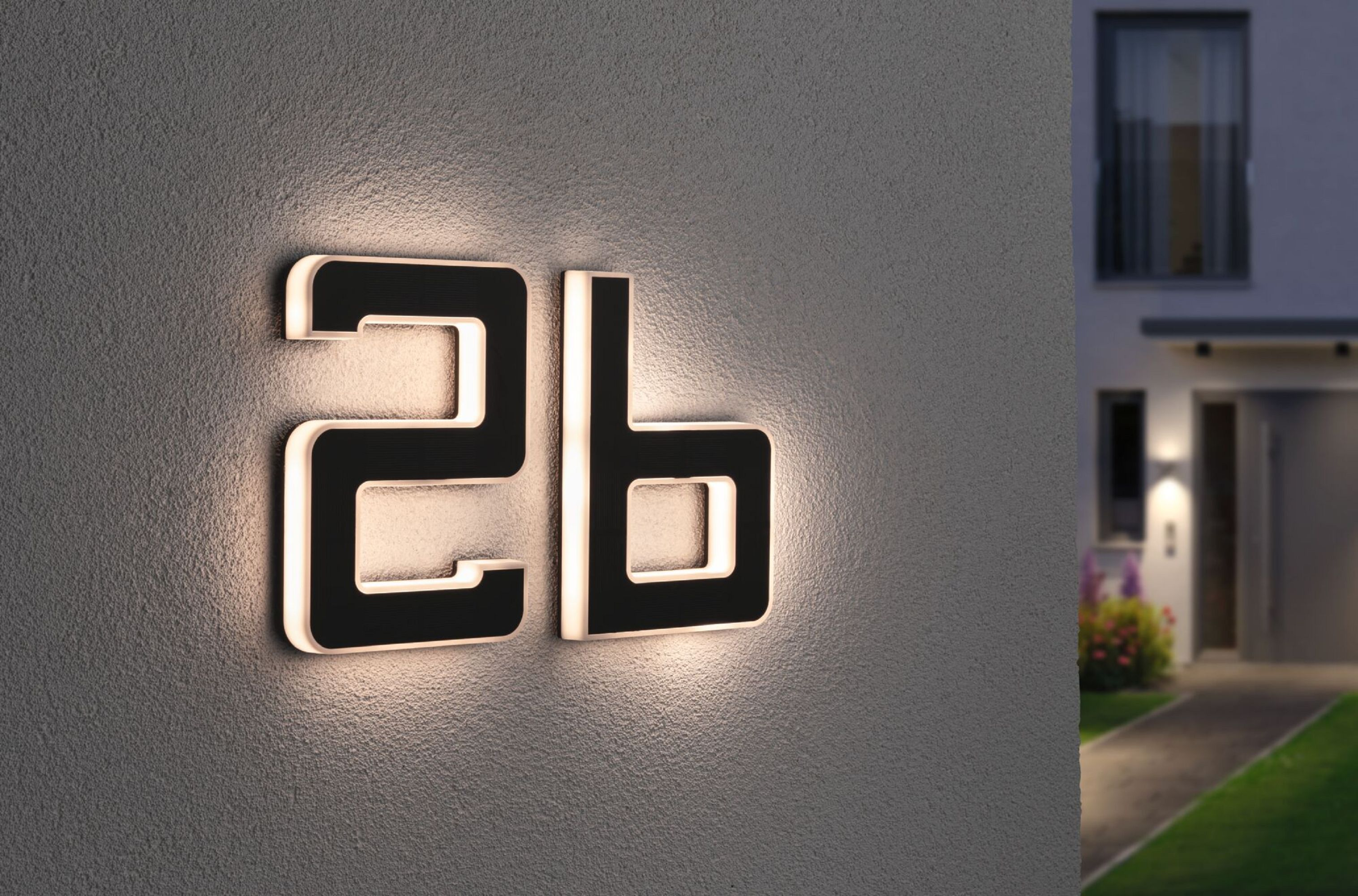 Podświetlone numery domów '2b' na szarej ścianie, z widocznym domem i światłami.