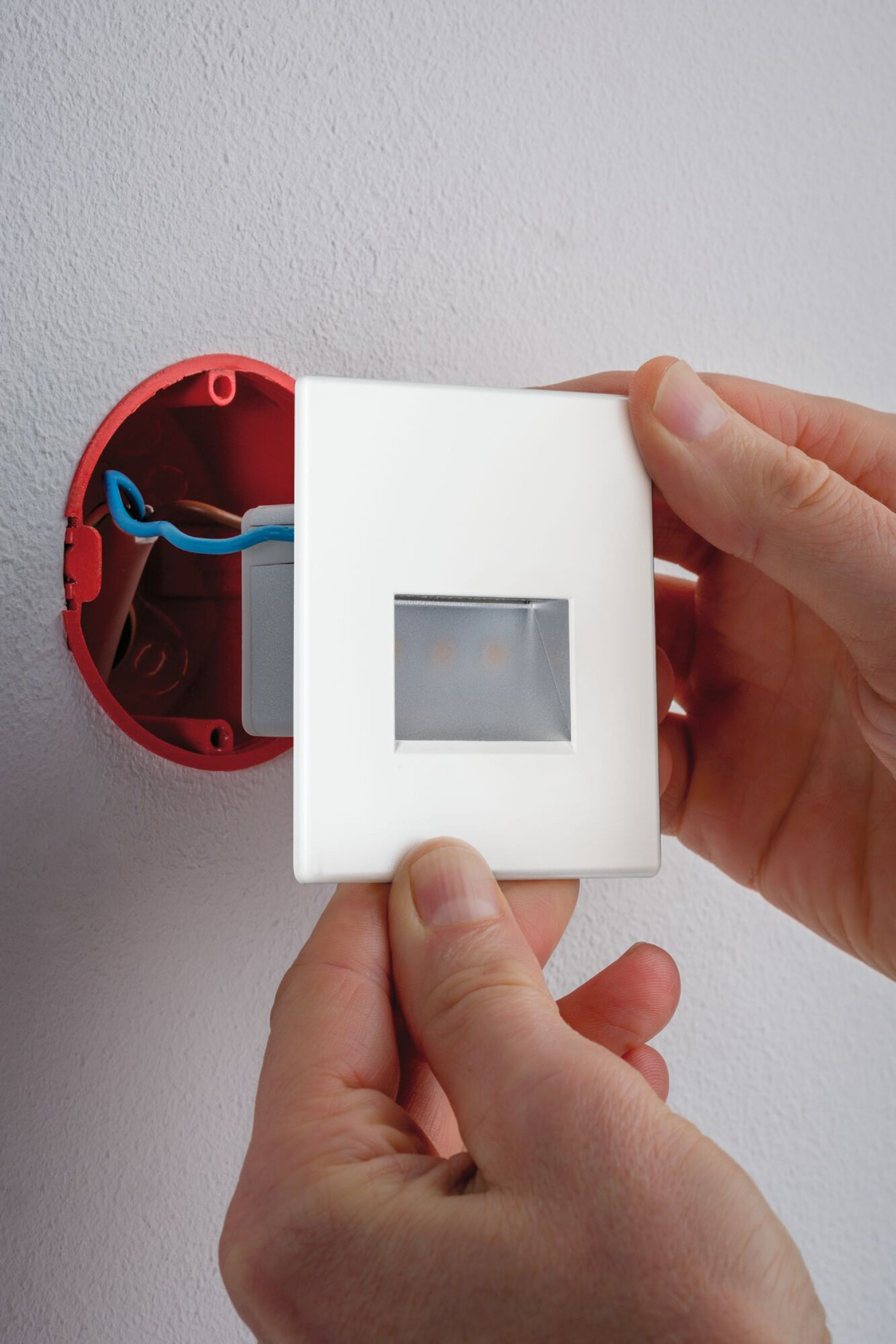 Ręce osoby trzymającej biały włącznik światła wewnątrz czerwonej skrzynki elektrycznej.