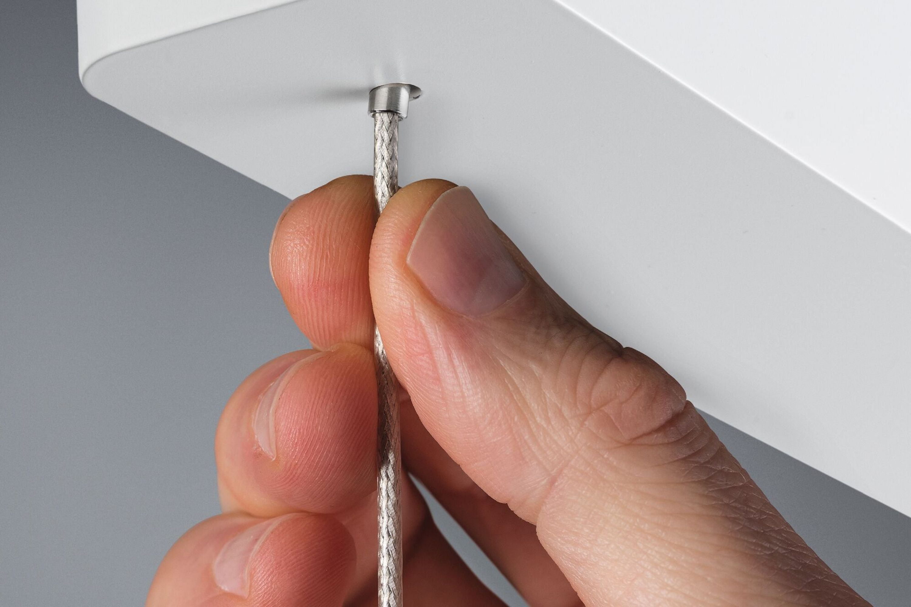 Ręka trzyma srebrny kabel, który jest przymocowany do białego elementu.