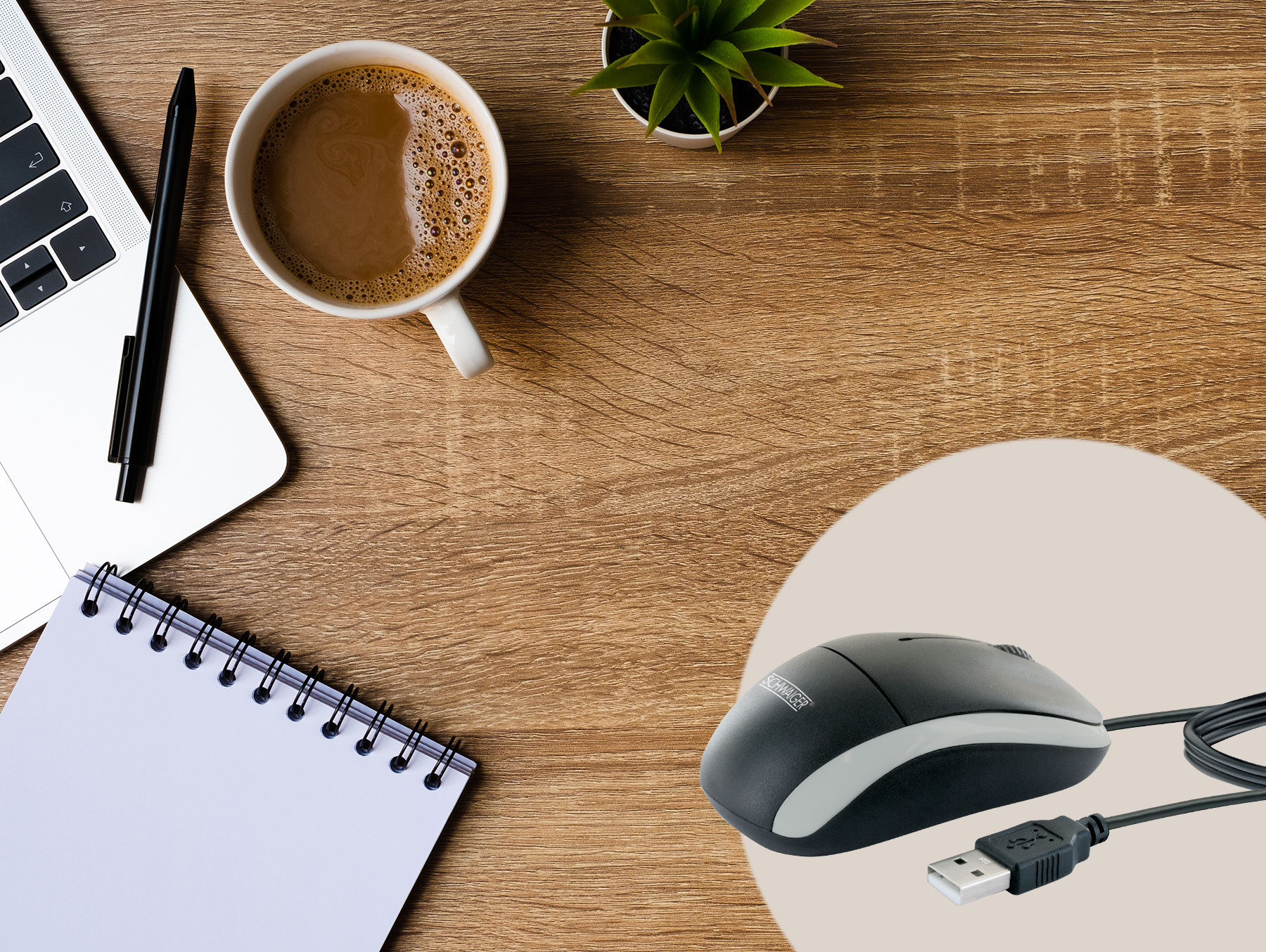 Ein Bürotisch mit Laptop, Kaffee, Notizbuch, Stift und einer Maus mit USB-Kabel.