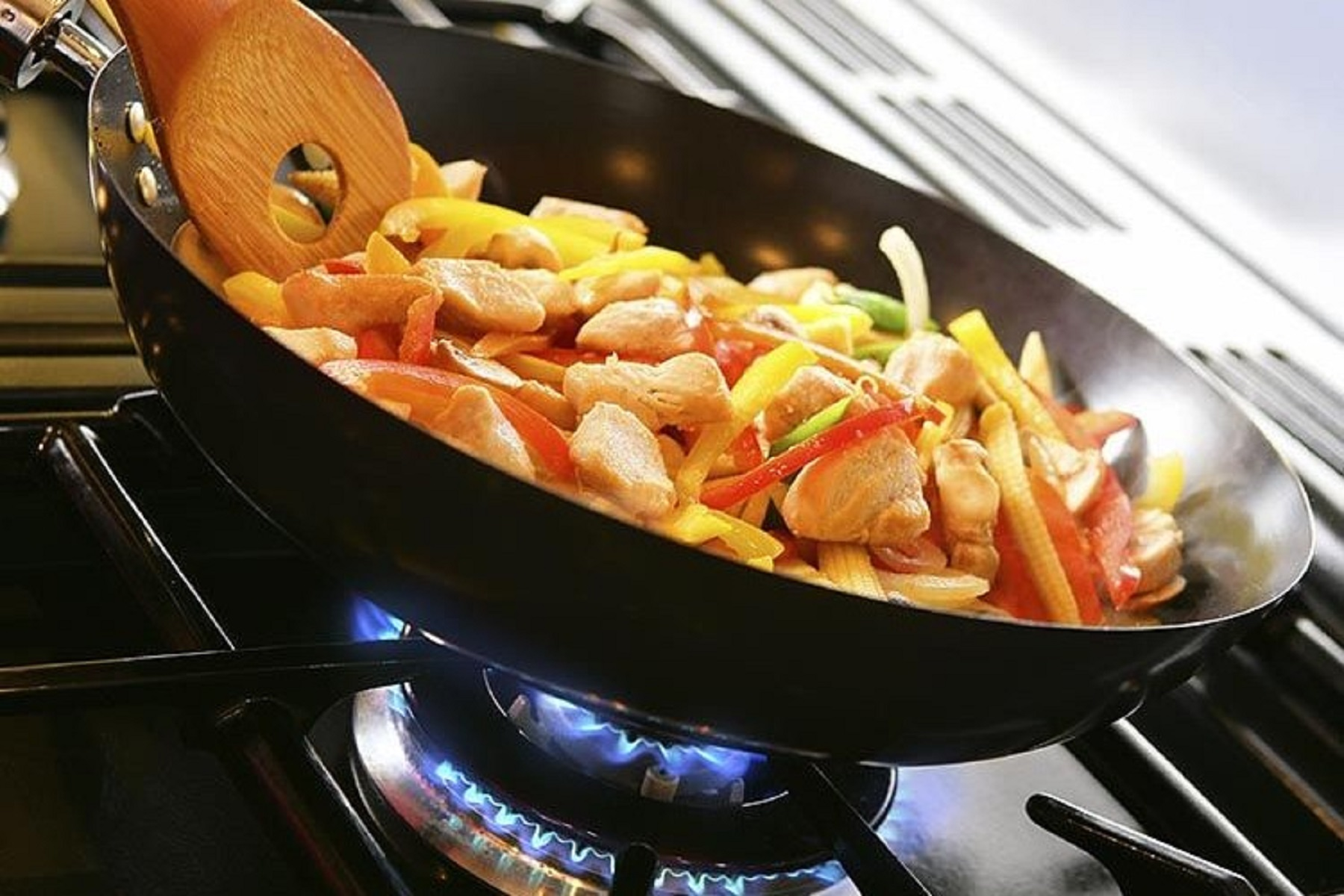 Wok con pollo y verduras, cocinando en una estufa de gas con llamas azules.