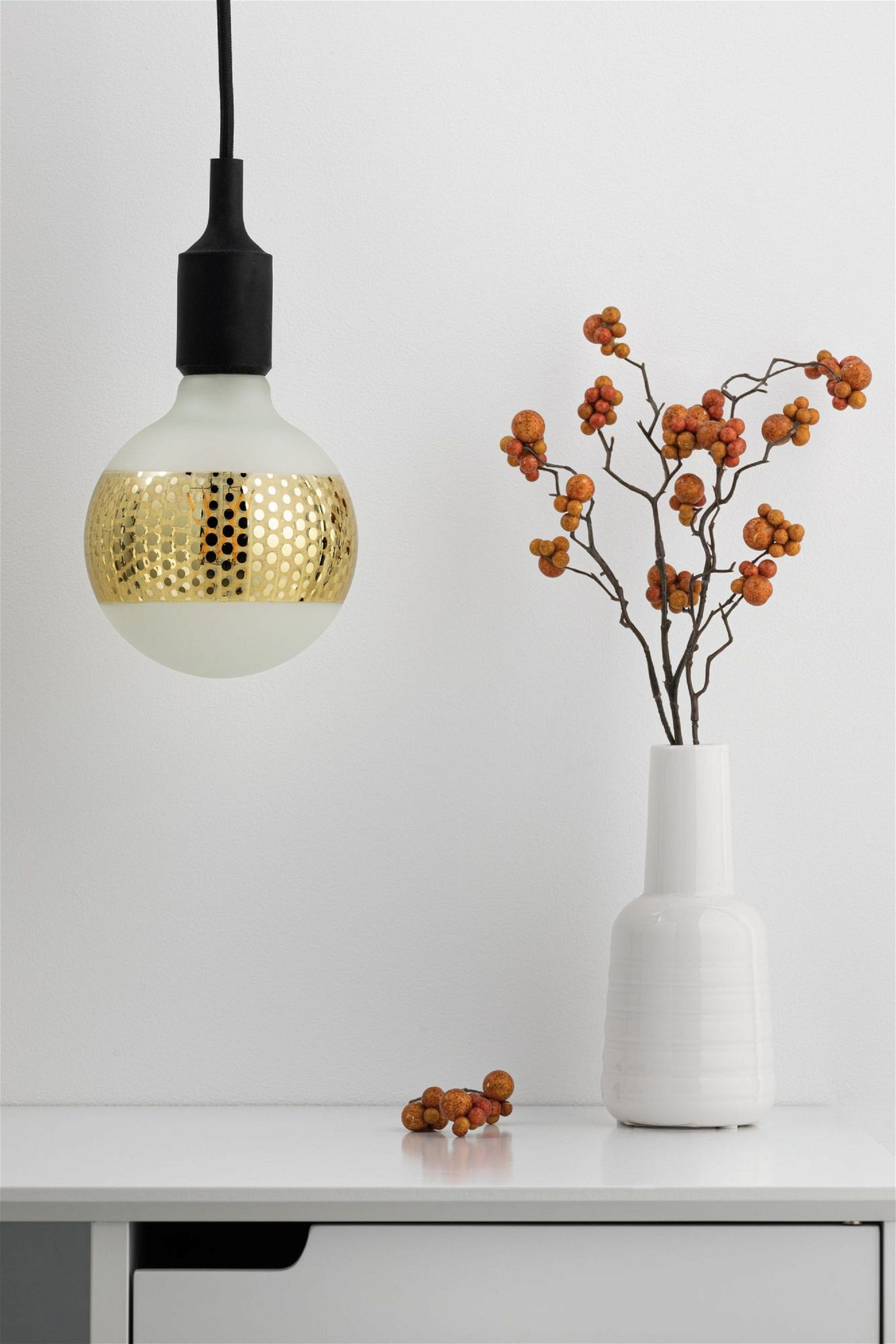 Lampadina rotonda con fascia dorata. Vaso bianco e ramo decorativo accanto.