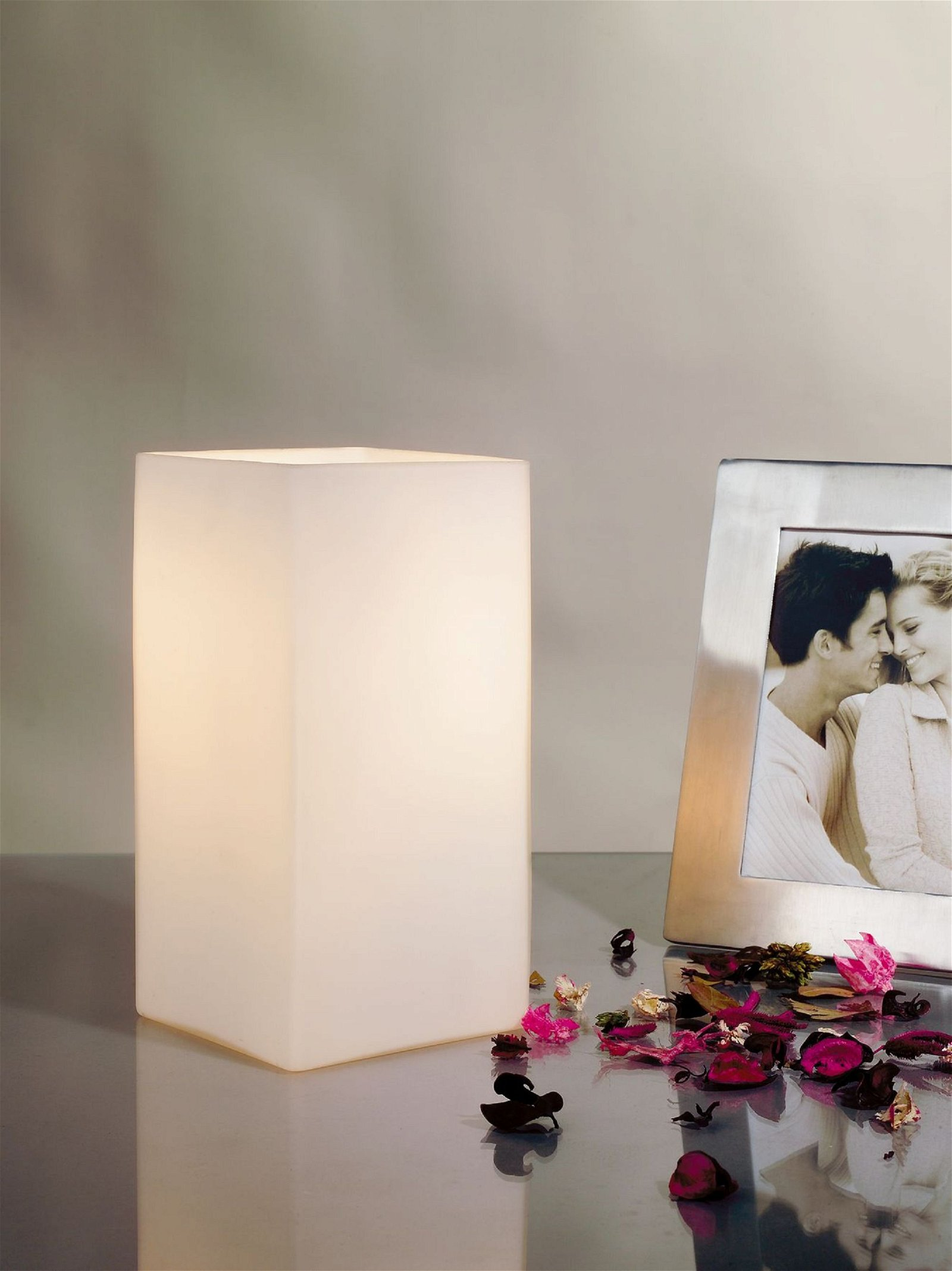 Biała lampa z ramką na zdjęcia i płatkami róż na stole.