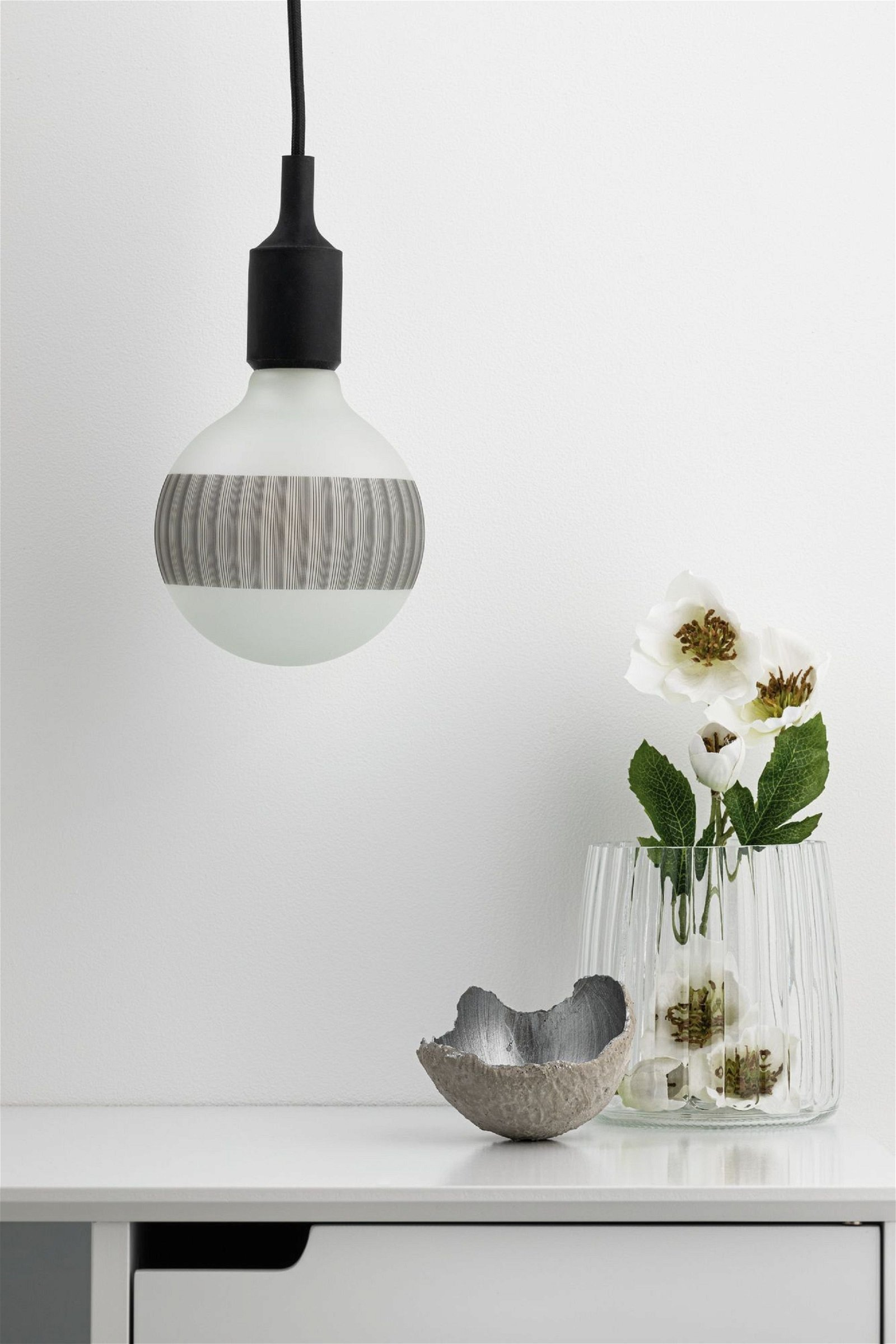 Eine Glühbirne mit Holzmaserung. Eine Vase mit Blumen steht neben einer grauen, strukturierten Schale.