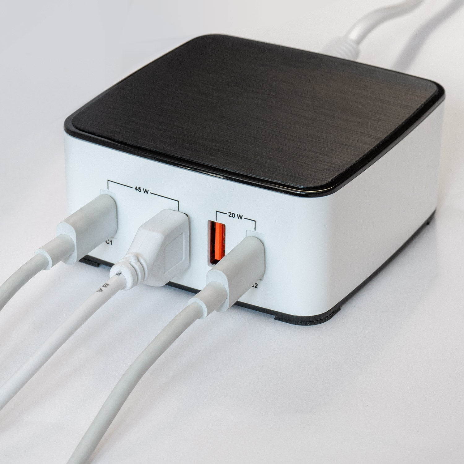 Ein schwarz-weißer Netzadapter mit drei eingesteckten USB-Kabeln auf einer weißen Oberfläche.